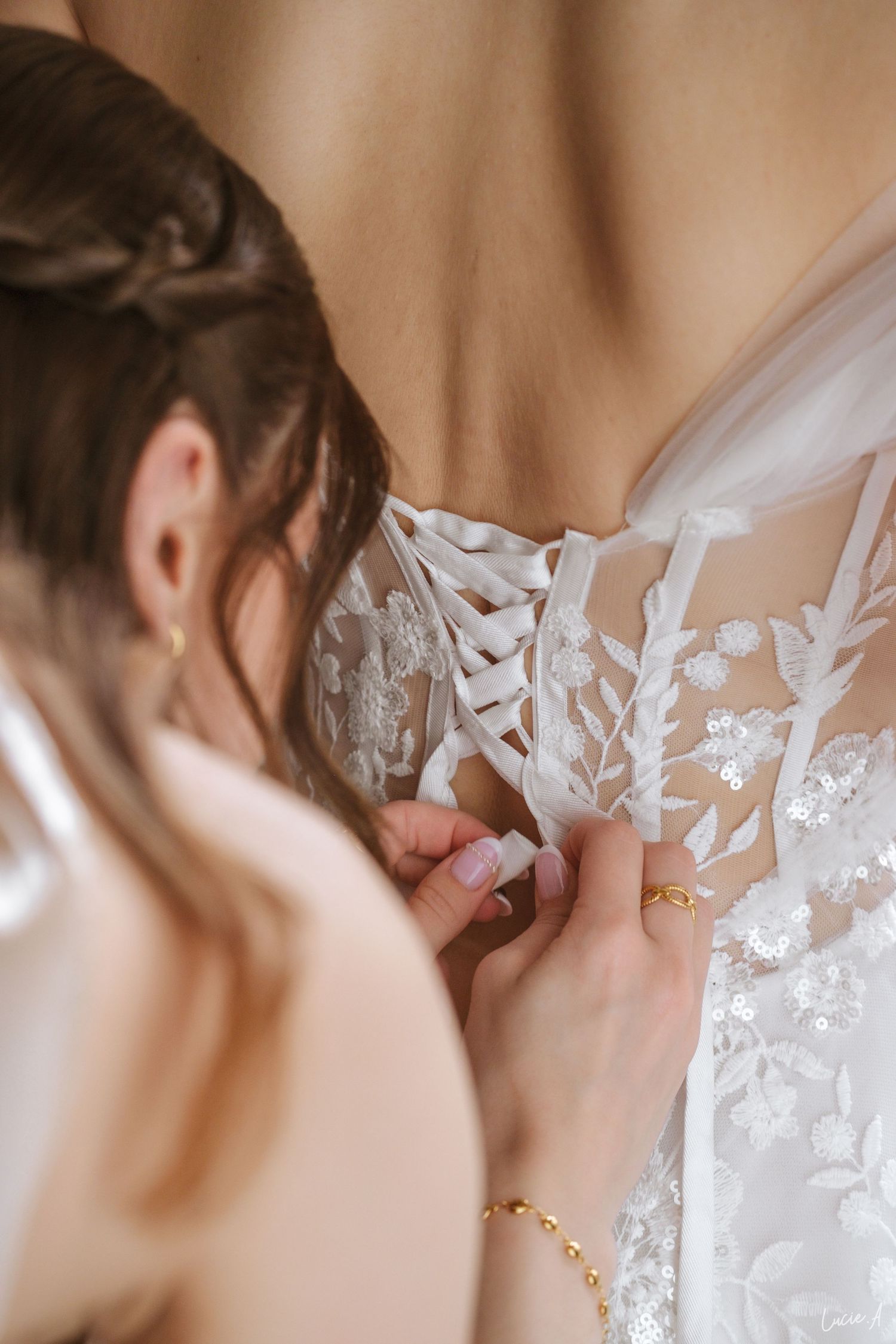 Une demoiselle d'honneur lace le dos d'une robe de mariée blanche en dentelle florale portée par la mariée avant la cérémonie.