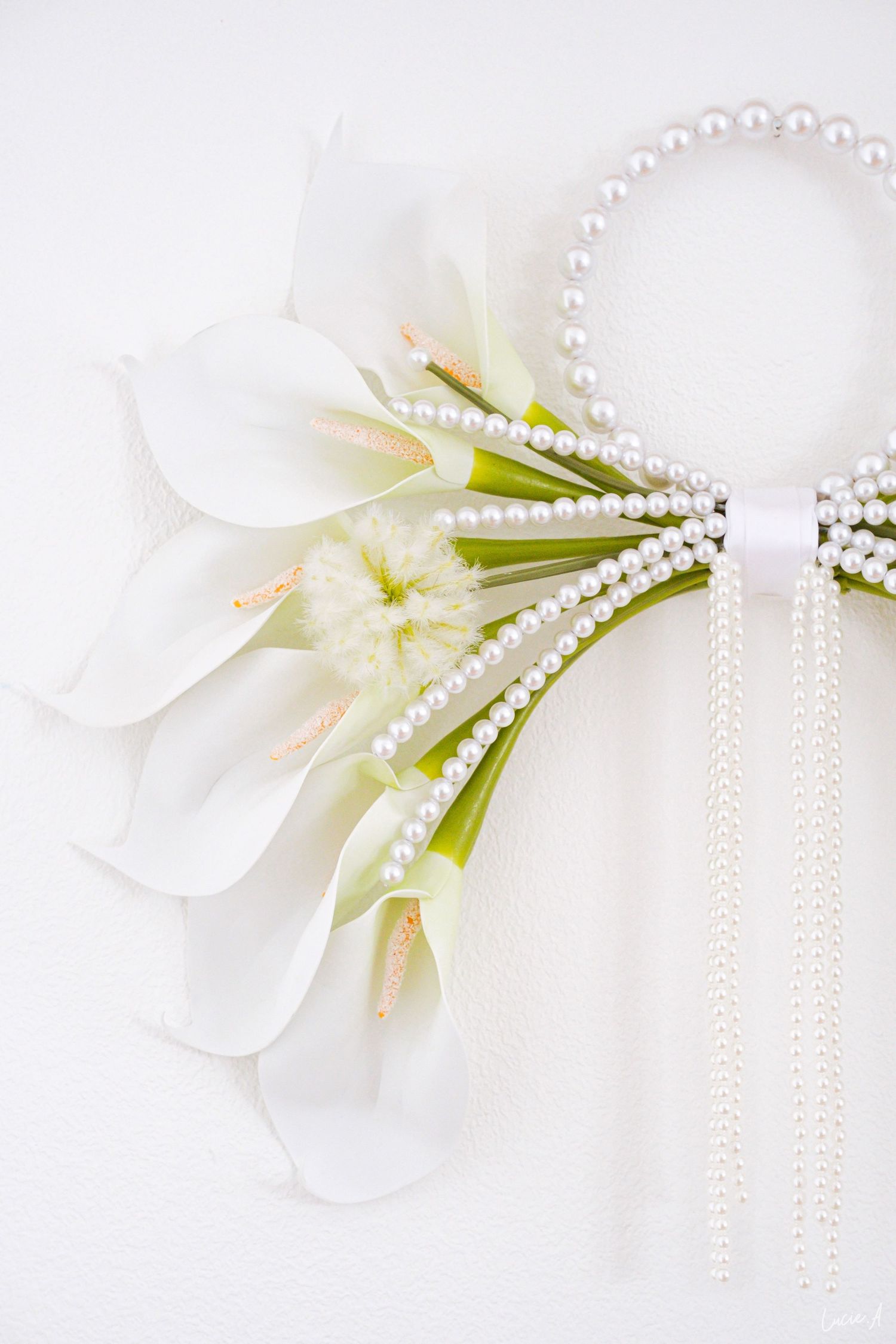 Élégant bouquet de mariée composé de callas blanches, orné de rangs de perles et d'un ruban blanc sur fond blanc.