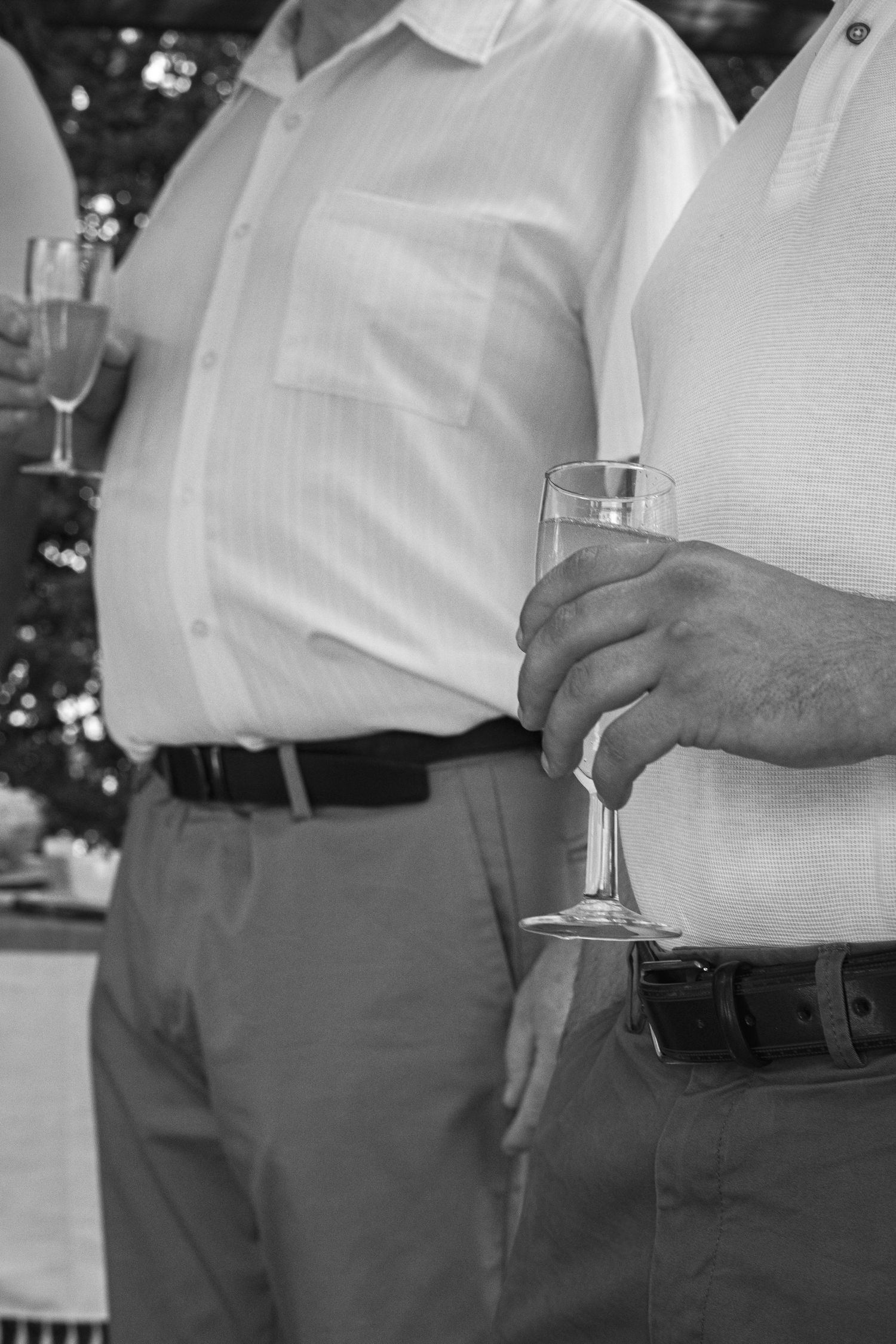 Black and white photo of two men in dress shirts holding champagne flutes at a formal outdoor gathering.