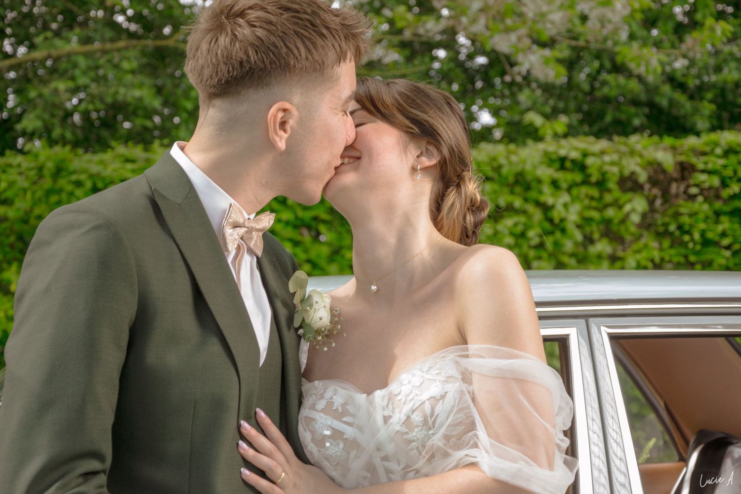 Les mariés échangent un baiser romantique à côté d'une voiture ancienne, entourés d'une végétation luxuriante.