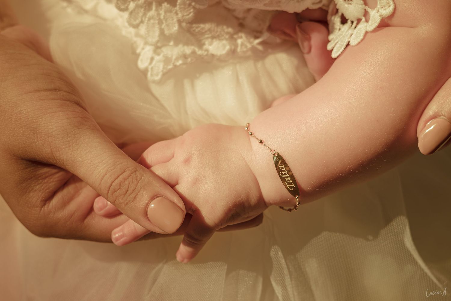 A newborn baby wearing a gold bracelet gently holds an adult's finger, symbolizing love and new parenthood.