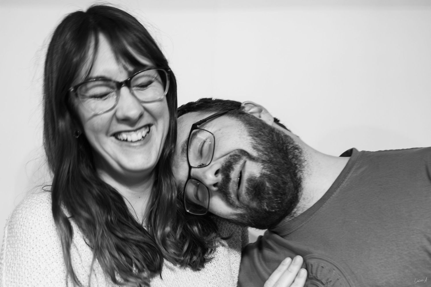 Photo en noir et blanc d'une femme riant, portant des lunettes, et d'un homme barbu posant sa tête sur son épaule.