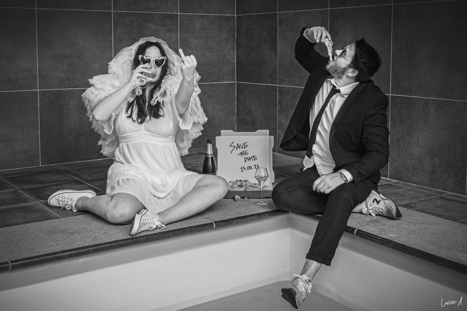 Photo en noir et blanc des mariés assis dans une baignoire, buvant et célébrant après la cérémonie de mariage.