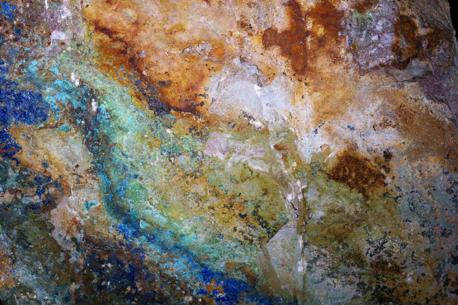 Close-up of colorful mineral rock surface with blue, green, gold, and rust tones creating an abstract natural pattern.