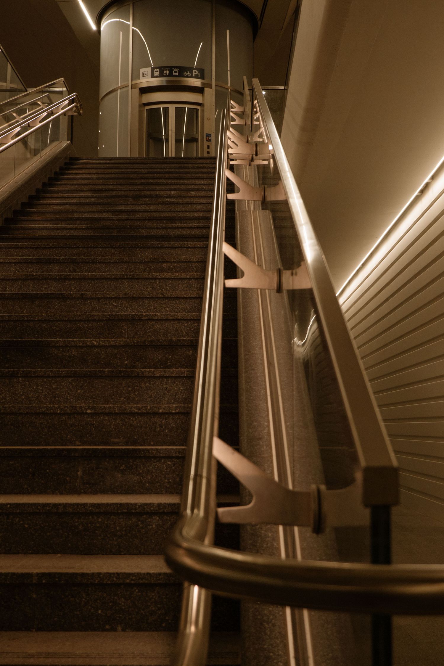 Escalier faiblement éclairé avec des rampes métalliques menant vers le haut dans une station de transit moderne, la nuit.