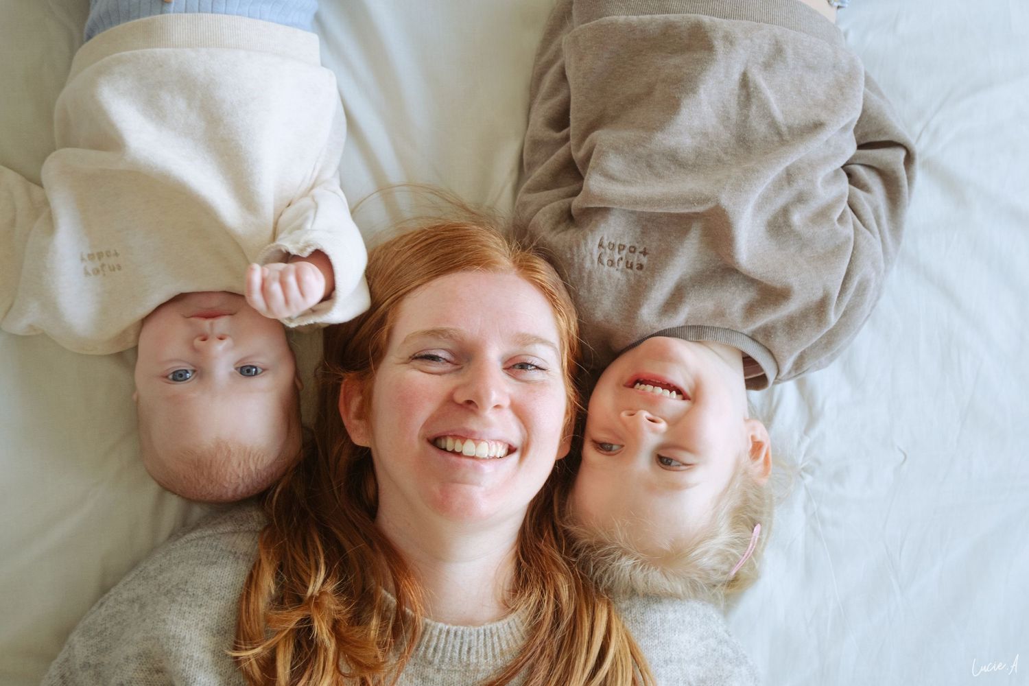 Portrait d'un famille réunissant une maman et ses deux enfants allongés sur un lit, tous souriants