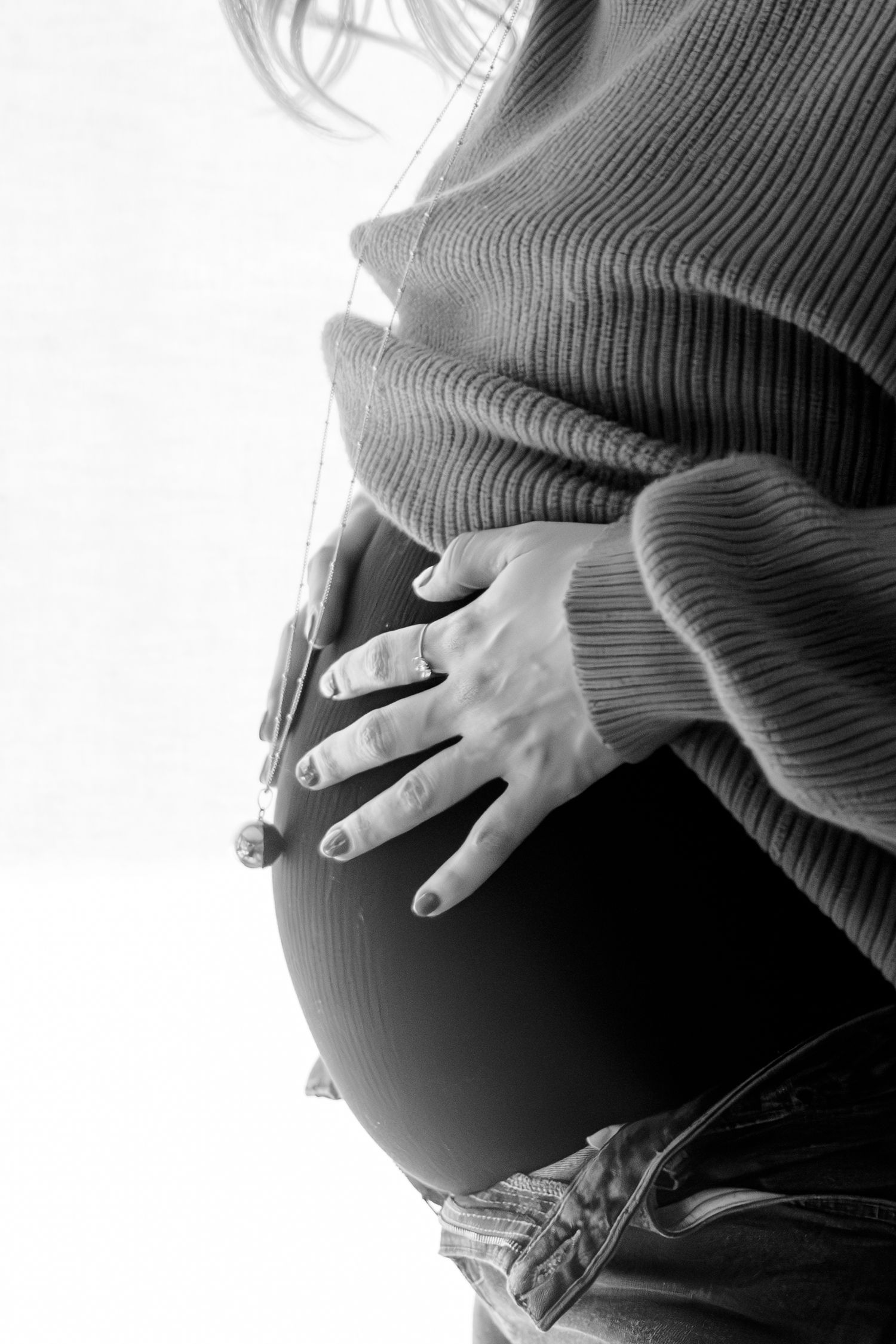 Portrait noir et blanc grossesse, gros plan de profil la mère posant ses mains sur son ventre, capté à Ronchin