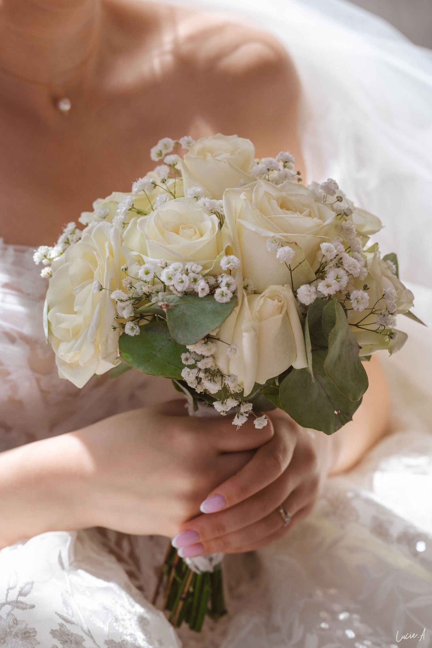 La mariée, vêtue d'une robe en dentelle, tient un élégant bouquet de roses blanches et de gypsophile.