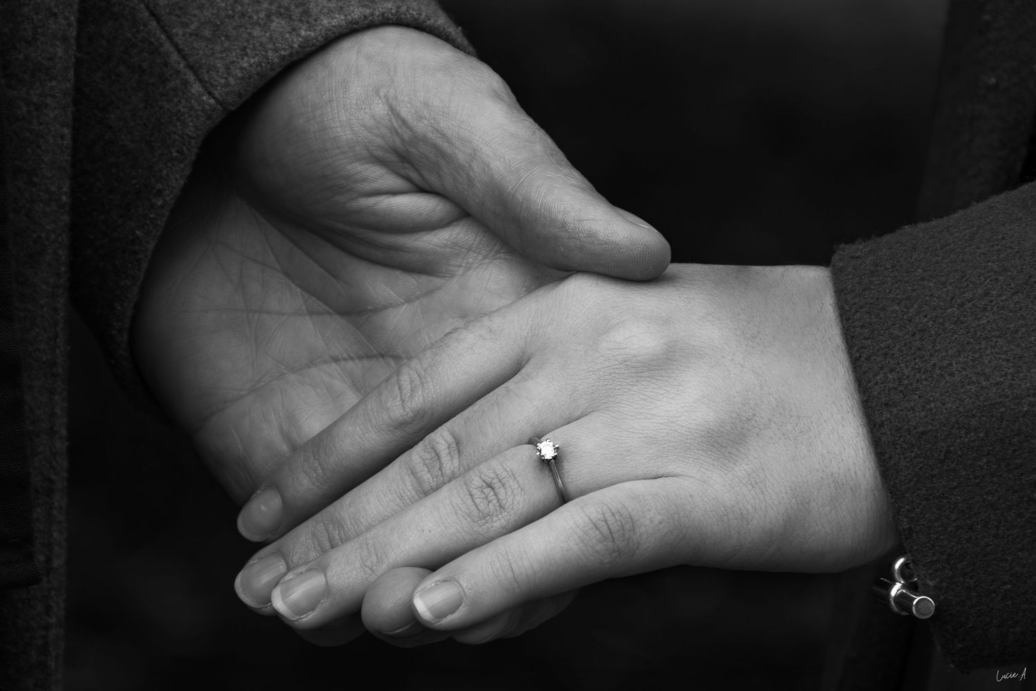 Gros plan noir et blanc sur les mains de deux fiancés se tenant du bout des doigts, bague de fiançaille mise en avant, à Lille