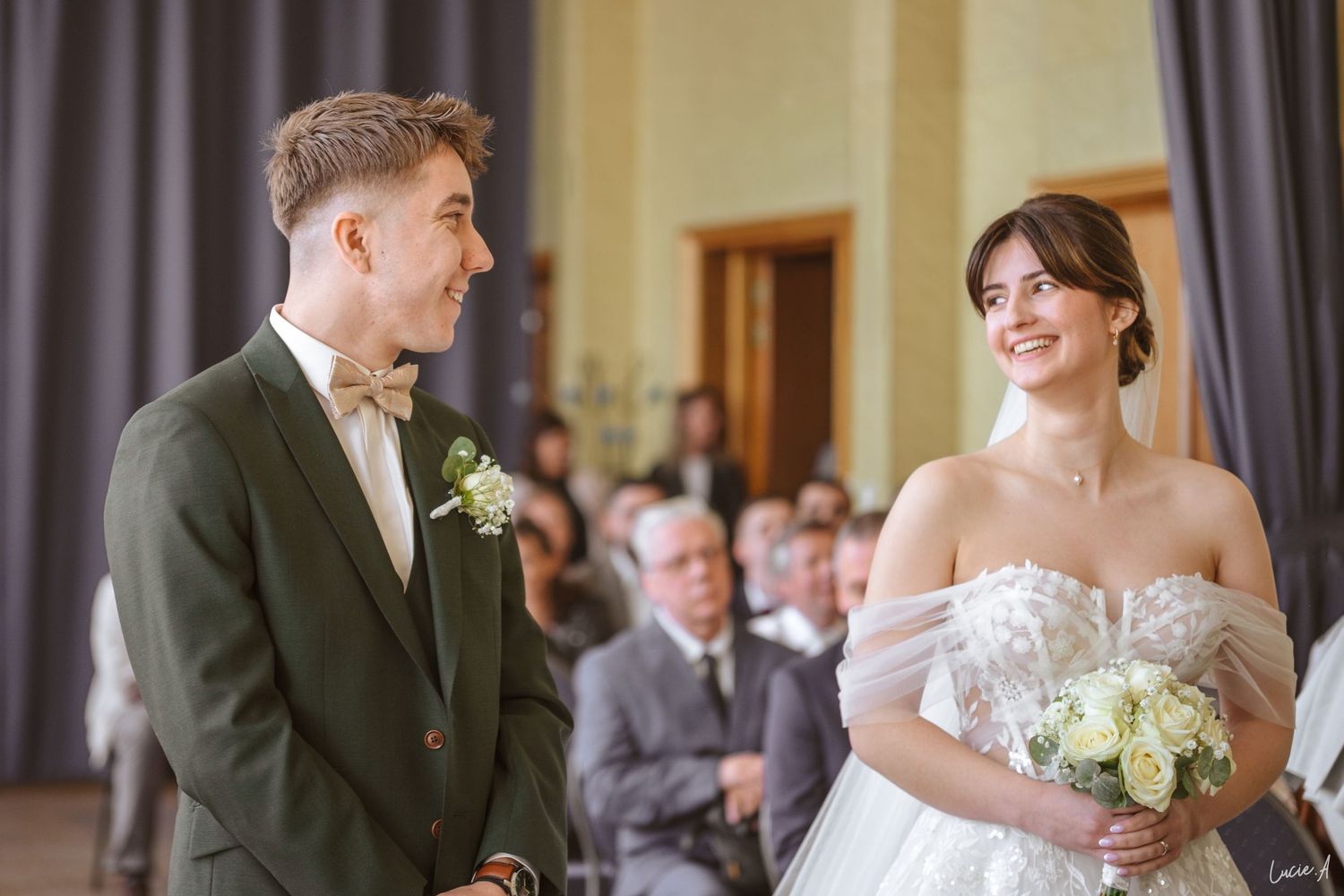 Les mariés se sourient pendant la cérémonie de mariage, la mariée tenant un bouquet de fleurs blanches dans une élégante robe de mariée.