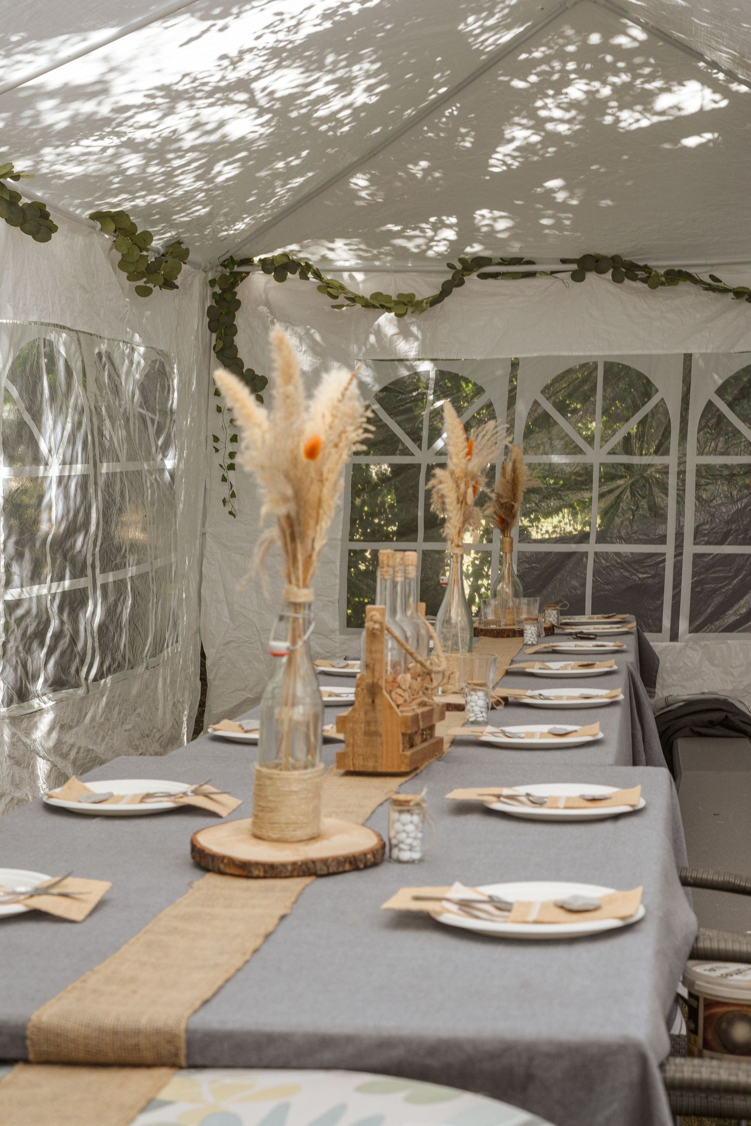 Élégante table de réception rustique dressée sous une tente chapiteau blanche, ornée de centres de table en herbe de la pampa et d'un chemin