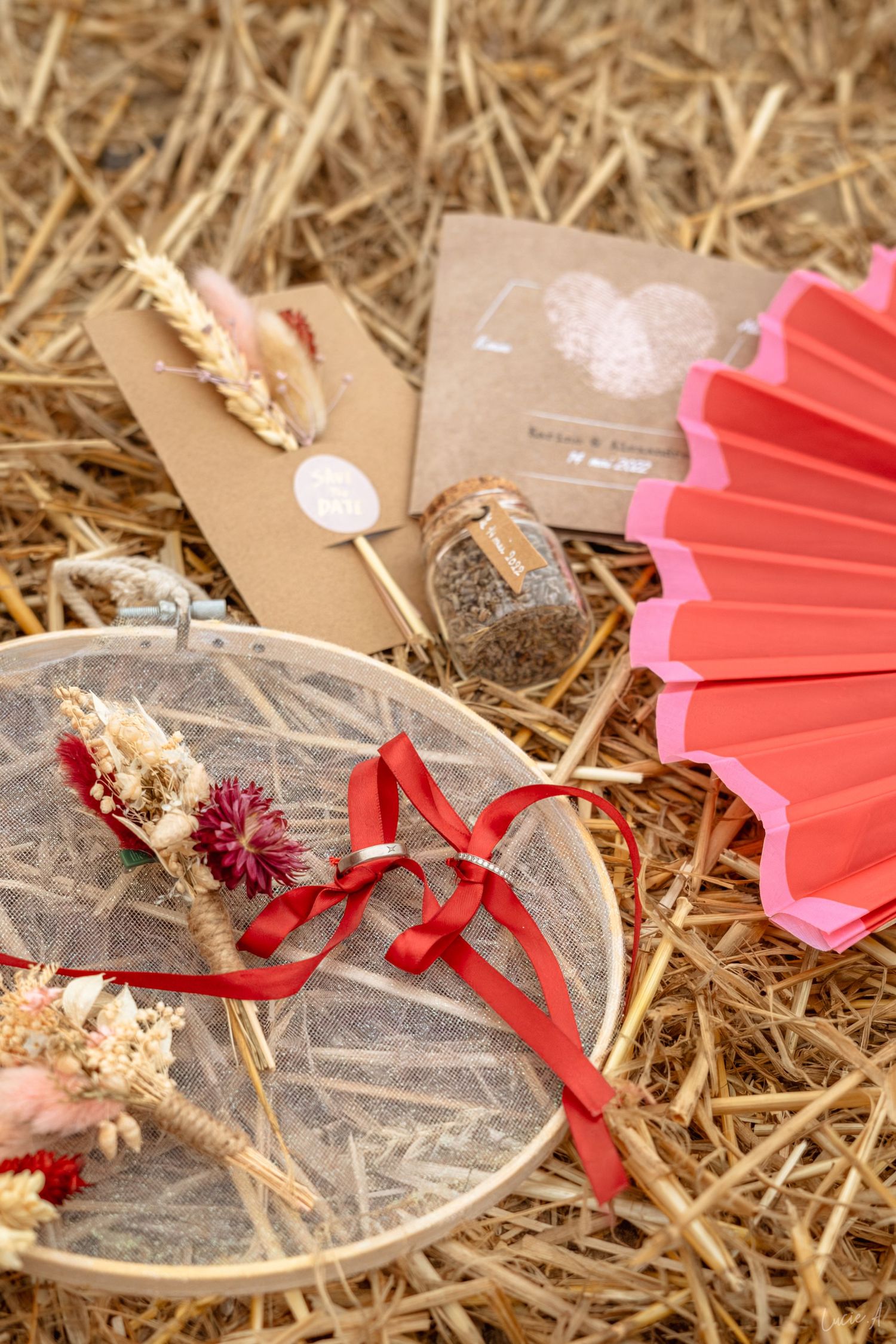 Composition champêtre à plat pour un mariage, avec éventail rouge, cercle à broder, fleurs séchées et invitations en papier kraft sur des bo