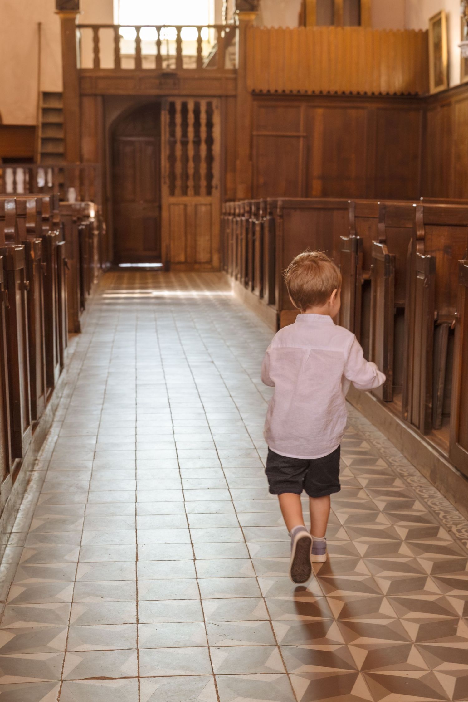 Young boy in white shirt and shorts running down the aisle of a wooden church interior.
