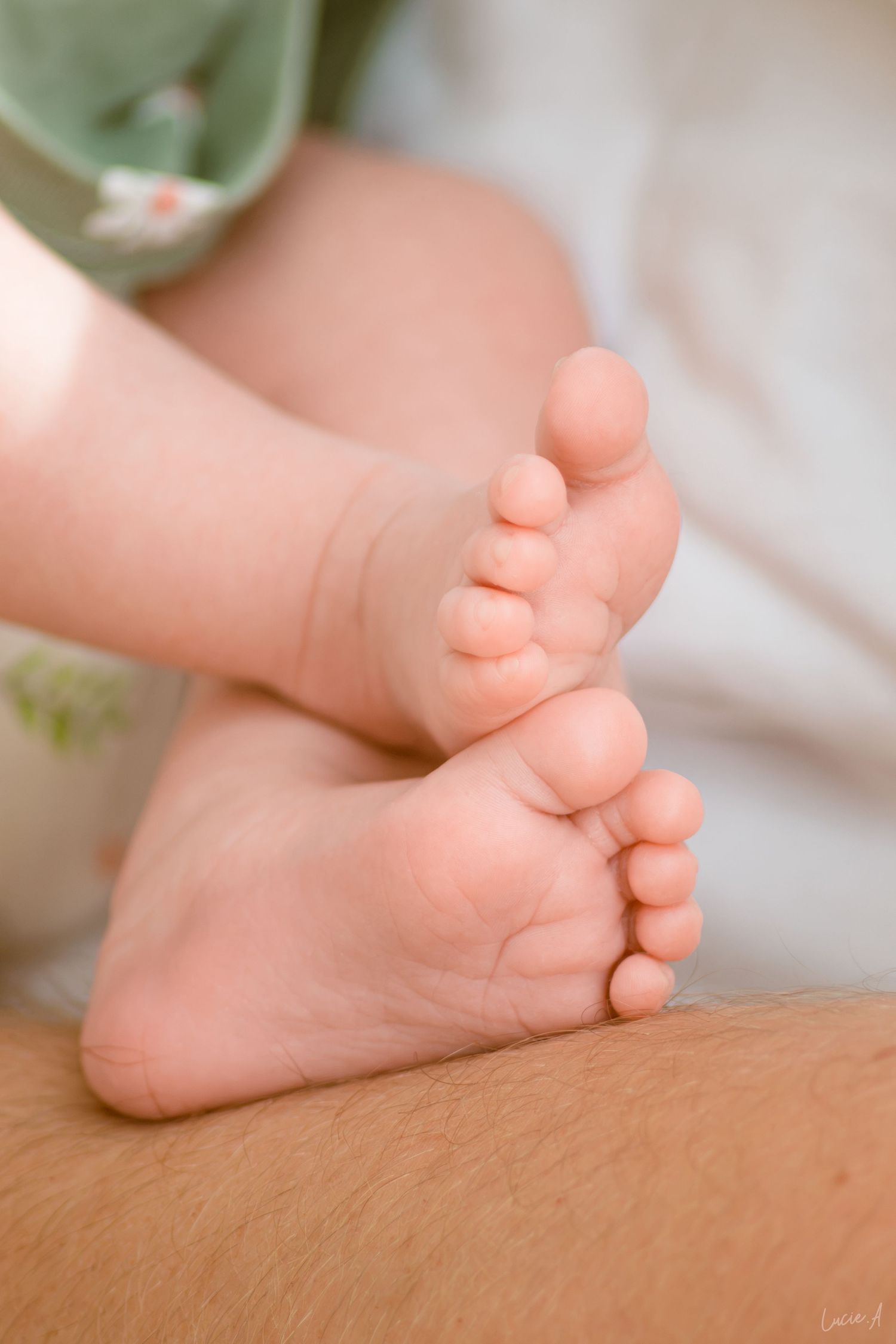 Gros plan sur les petits pieds d'un nouveau-né posés sur la main d'un adulte, vêtu d'une tenue verte à fleurs.