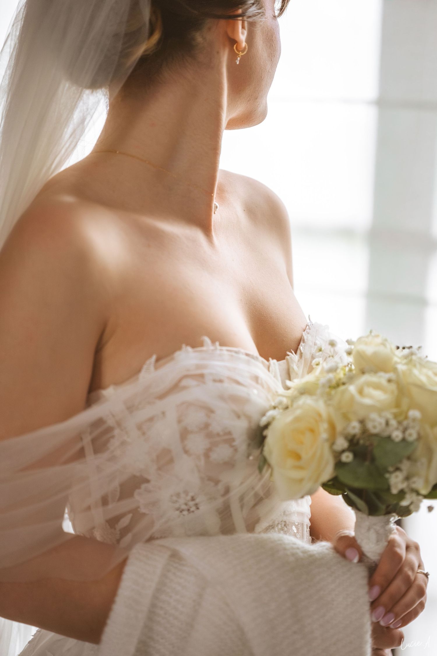 Élégante mariée en robe de mariée bustier en dentelle, tenant un bouquet de roses blanches et portant un voile, photographiée de dos.