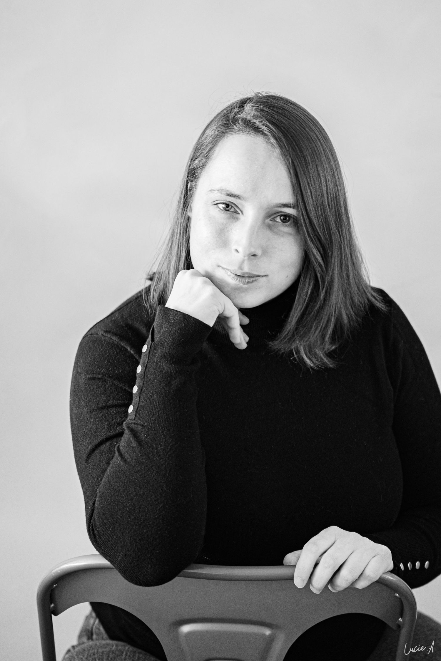 Portrait noir et blanc d’une jeune femme en pull à col roulé, posant son menton sur sa main alors qu’elle est assise. séance corporate