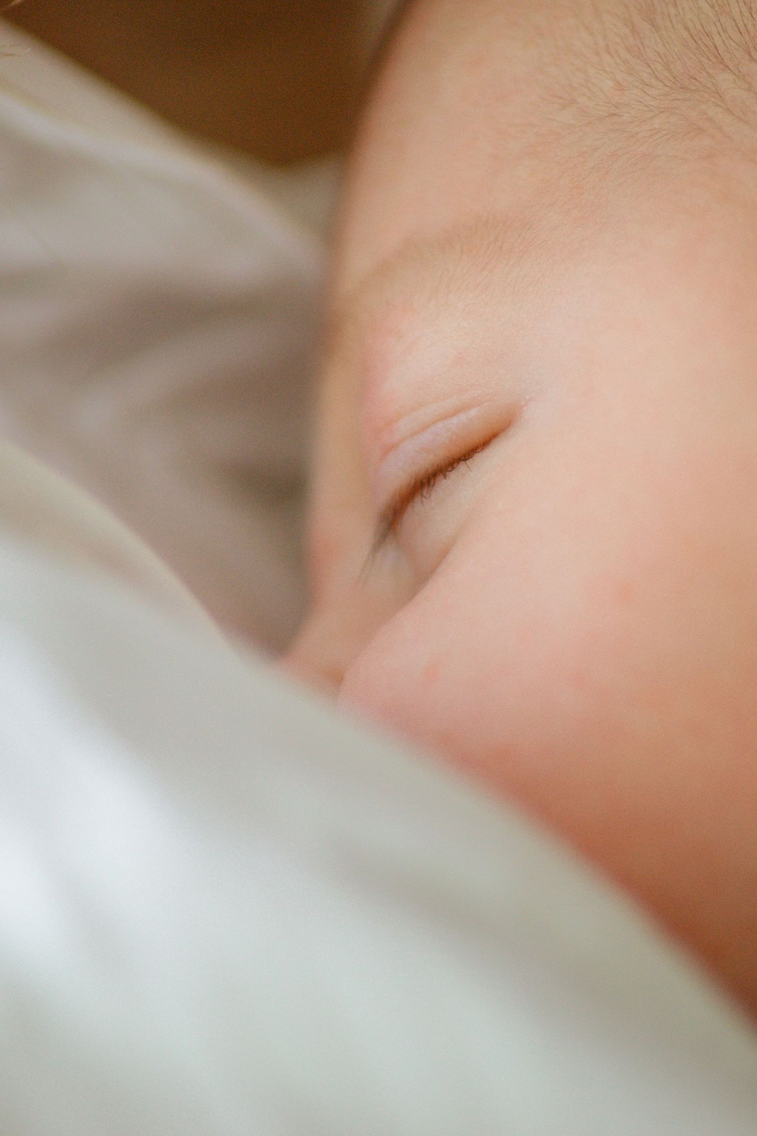 Close-up of a sleeping newborn baby's face resting peacefully on soft white bedding.