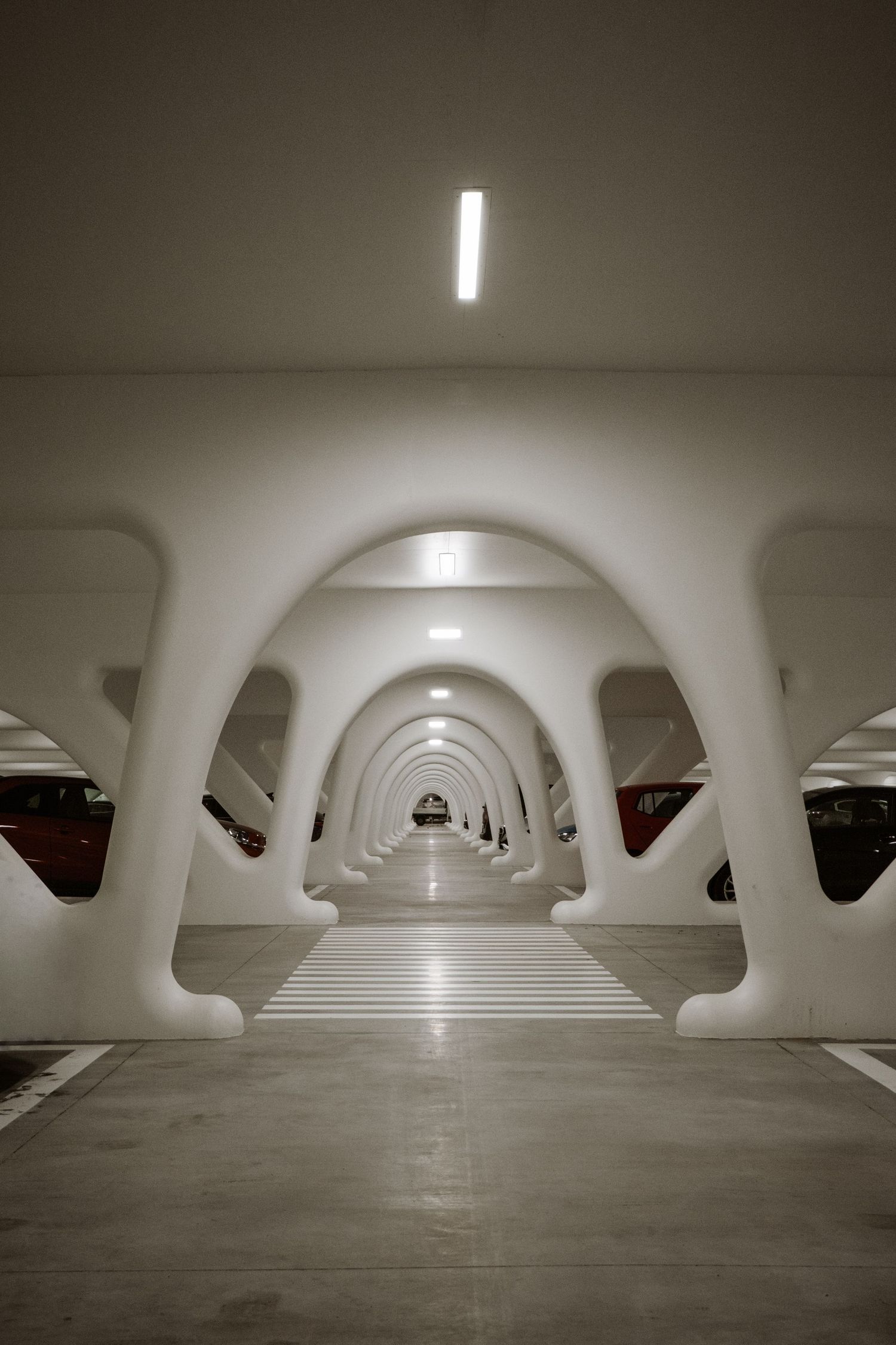 Couloir futuriste blanc voûté dans un parking moderne, avec des arches répétées créant une perspective spectaculaire.