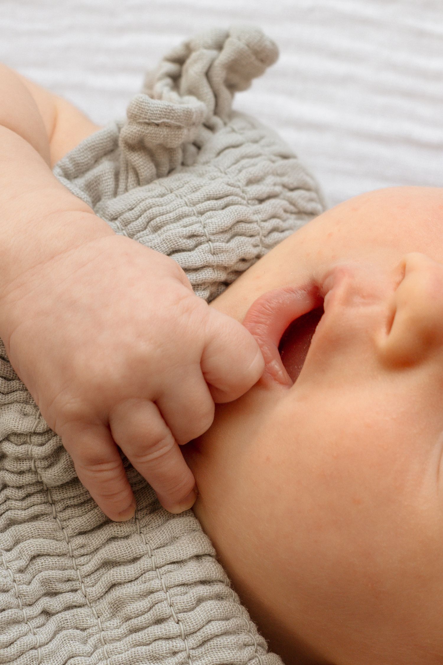 Close-up of a sleeping newborn baby wearing a gray knit hat, with tiny hand resting on chest.