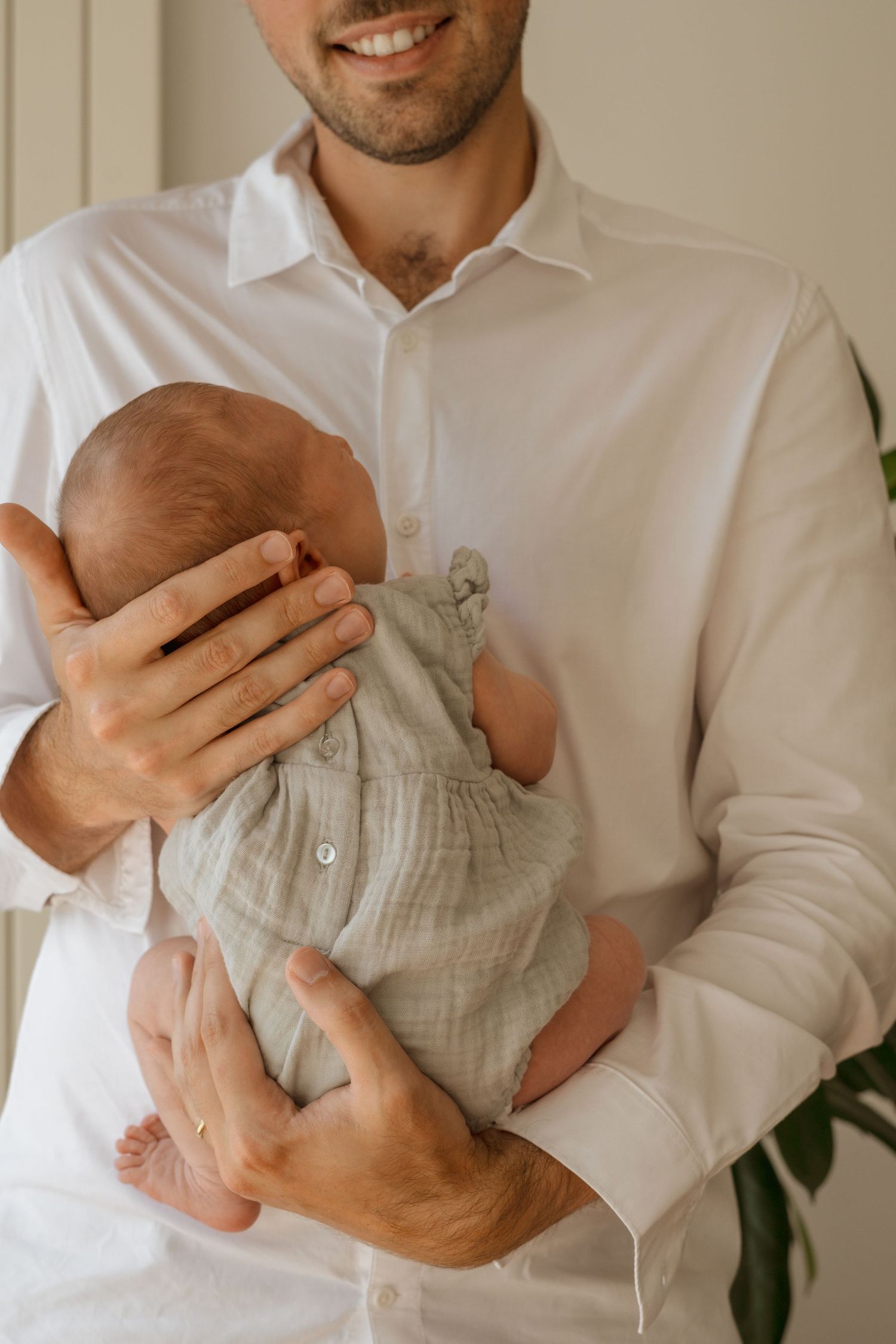Smiling father in white shirt tenderly holding a newborn baby dressed in a soft sage green outfit.