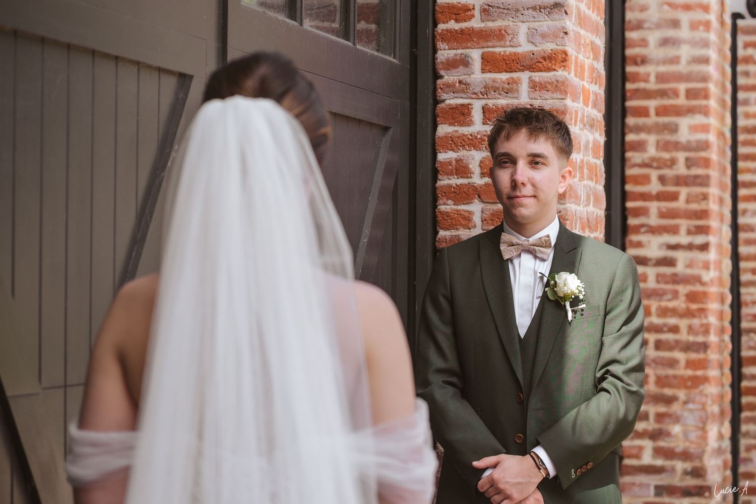 Le marié, vêtu d'un costume vert olive, adresse un sourire chaleureux à la mariée lors de ce moment d'émotion où ils se découvrent.