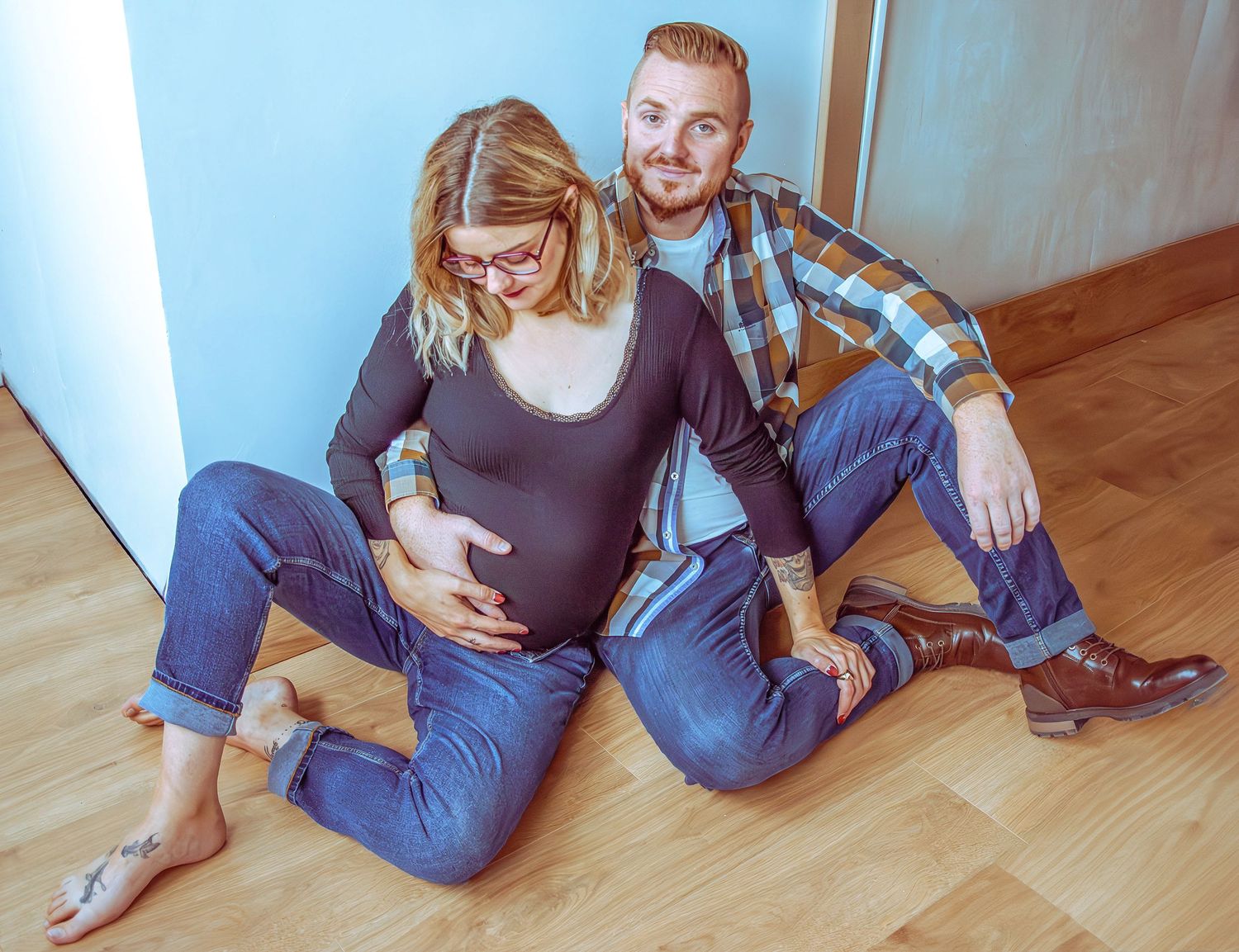 Portrait séance grossesse, couple assis, le futur père posant la main sur le ventre de la future mère, capté à Ronchin près de Lille