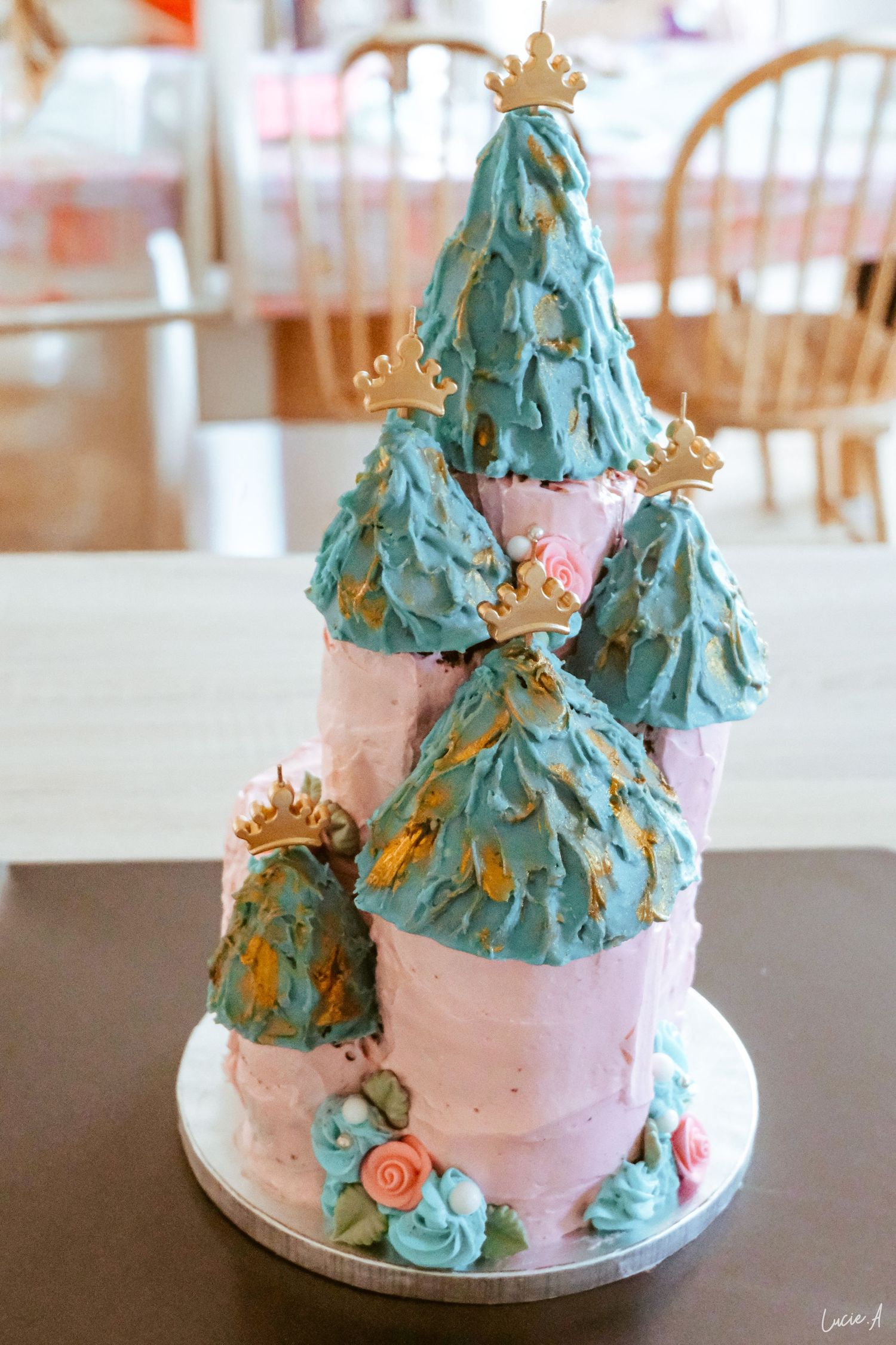 Gâteau d'anniversaire élégant en forme de château de princesse, avec des étages roses, des tours de glaçage turquoise, des couronnes dorées