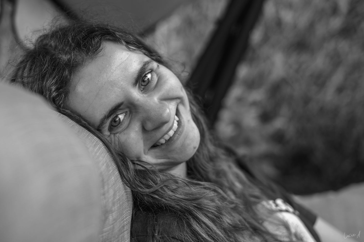 Portrait en noir et blanc d'une jeune femme souriante aux longs cheveux reposant sur sa tête, regardant l'objectif.