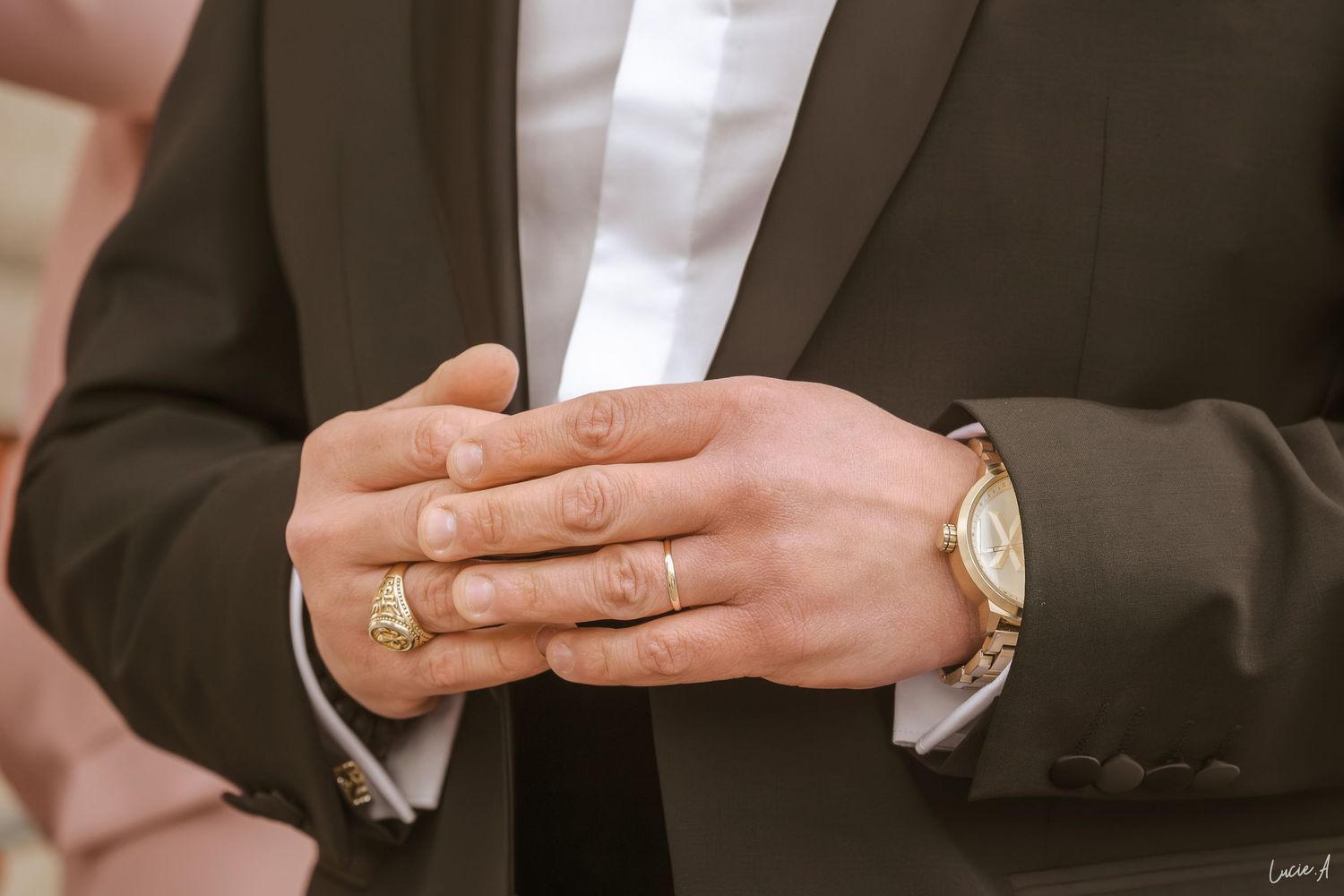 Gros plan sur les mains d'un marié portant une alliance en or et une montre de luxe en or, vêtu d'un costume sombre.