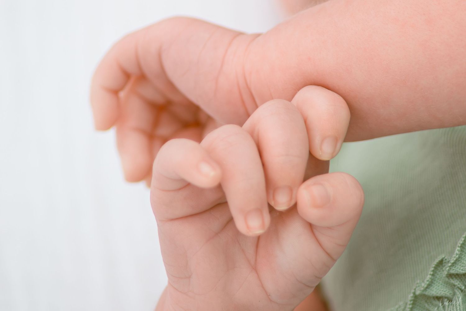 Gros plan sur la minuscule main d'un bébé serrant délicatement le doigt d'un adulte vêtu de vert.