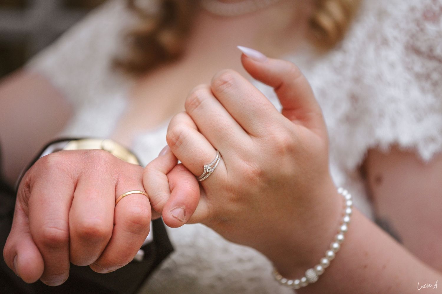 Gros plan sur des jeunes mariés se tenant la main, tous deux portant des alliances en or, la mariée portant un bracelet de perles.