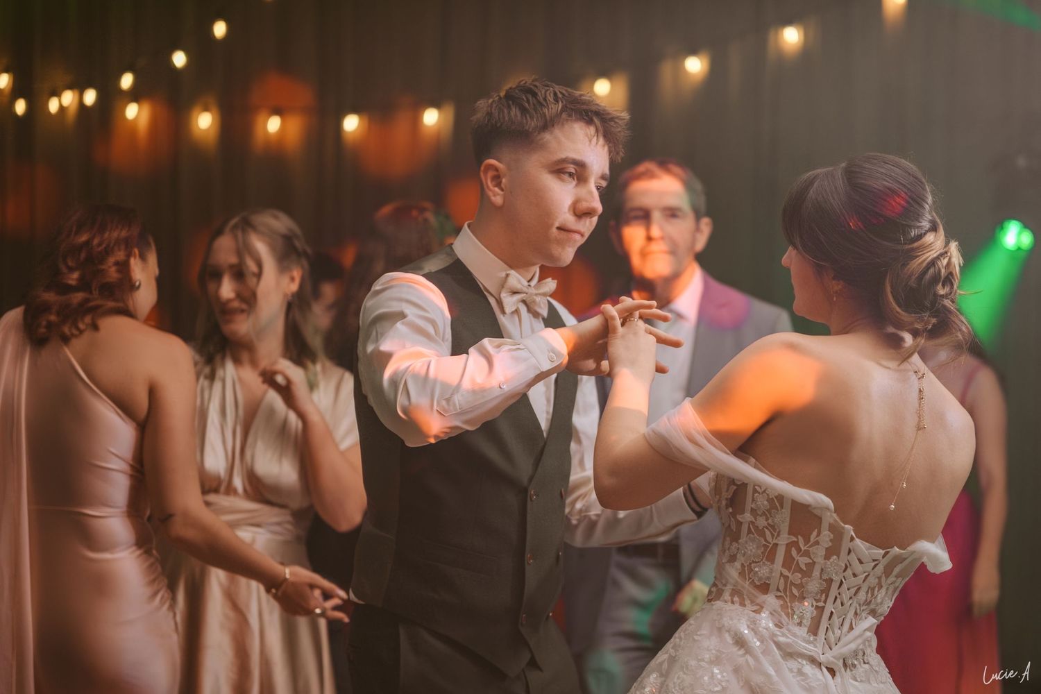Le marié danse avec la mariée, vêtue d'une robe corset blanche, lors de la réception de mariage sous le regard des invités.