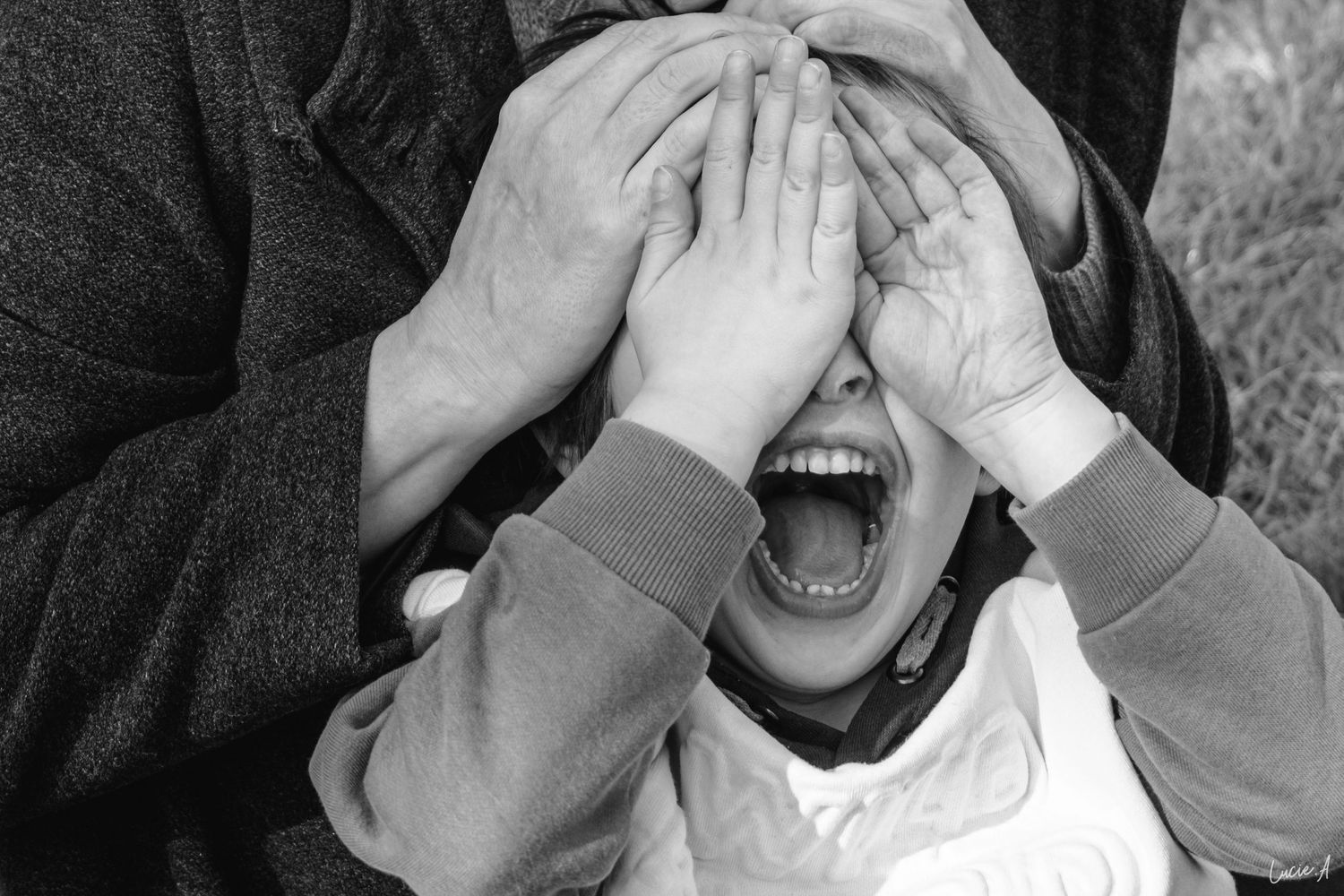 Portrait en noir et blanc d'une maman et de son fils, l'enfant se cache les yeux en souriant