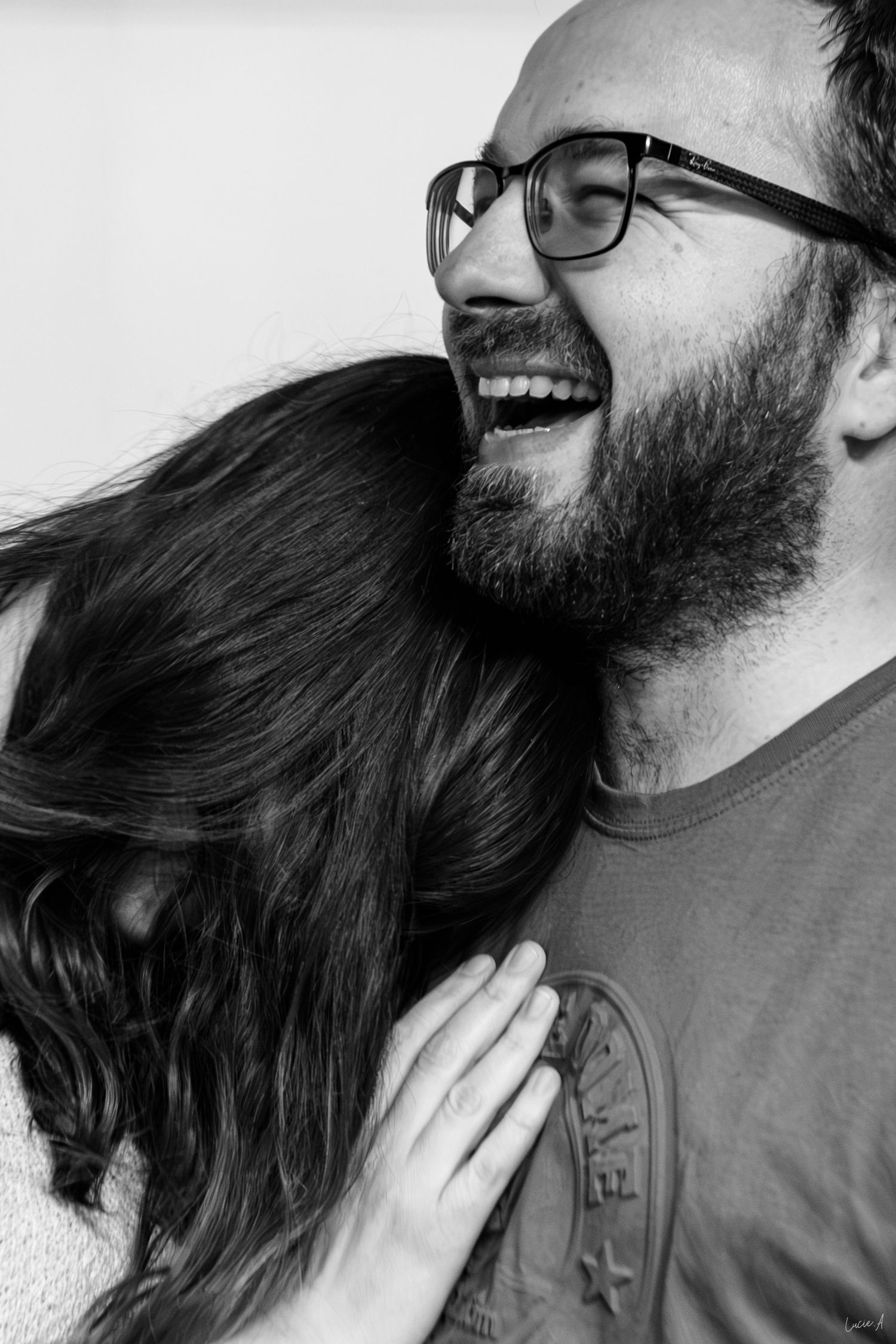 Photo en noir et blanc d'un homme barbu riant et portant des lunettes, enlaçant une femme aux cheveux noirs appuyée sur son épaule.