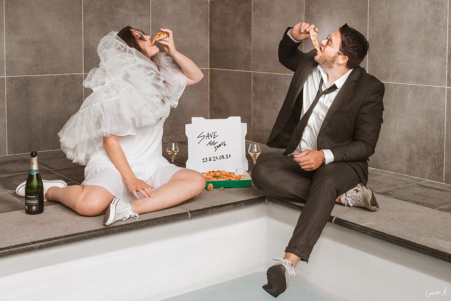 Les mariés, assis au bord d'une piscine, mangent des pizzas et boivent du champagne après leur cérémonie de mariage.
