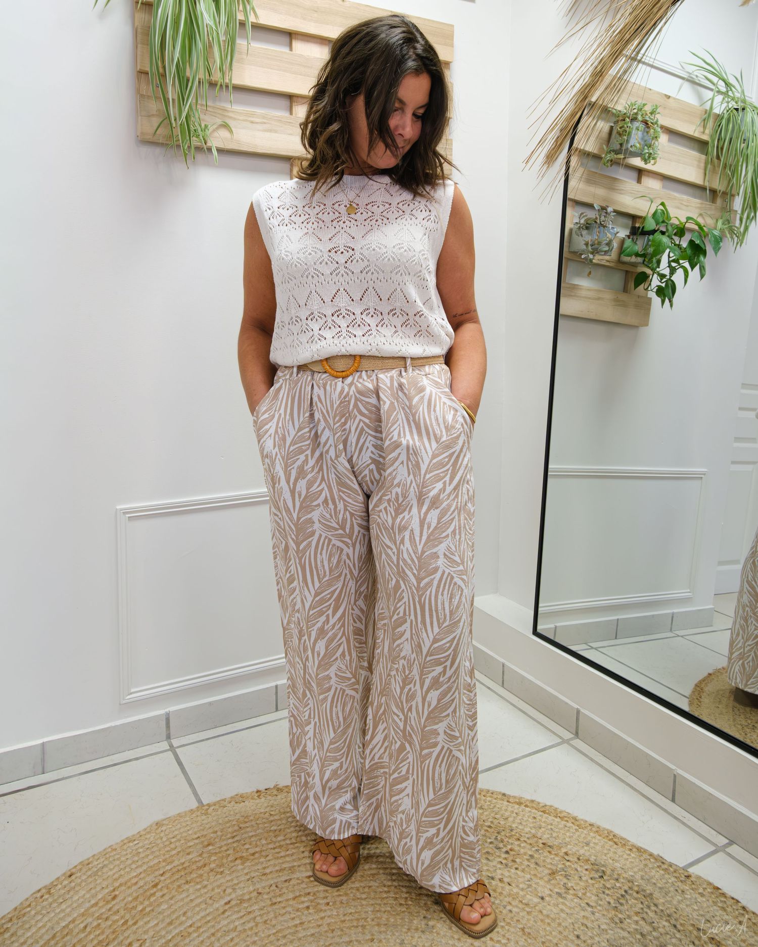 Femme portant un pantalon fleuri à jambes larges et un haut en dentelle sans manches dans des tons neutres, debout dans une pièce d'un blanc