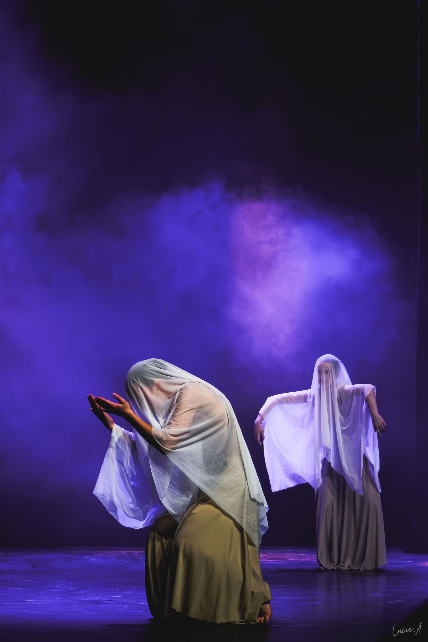 Deux artistes drapés de tissu blanc sur une scène sombre, baignée de fumée violette, lors d'une représentation de danse théâtrale.