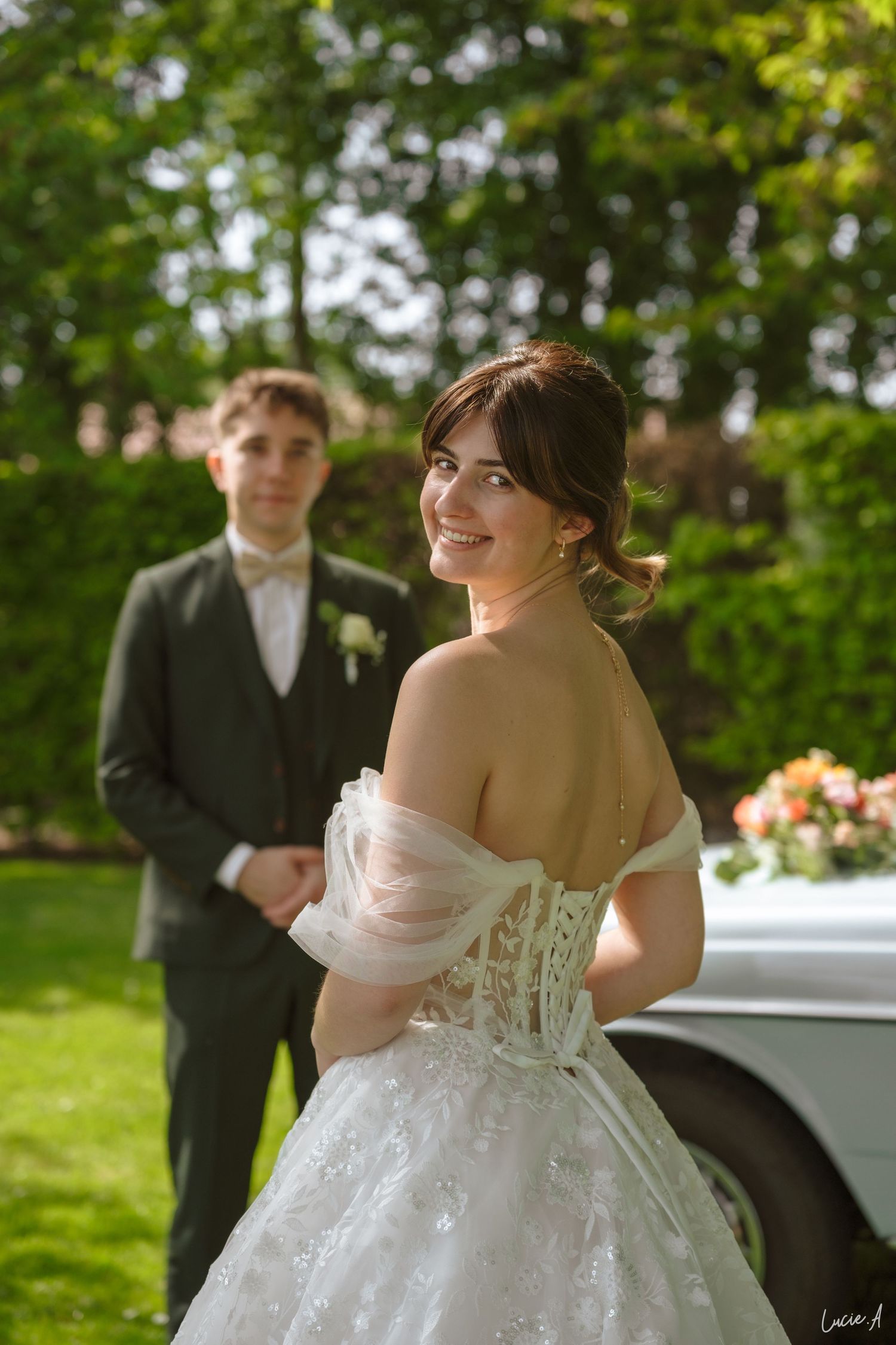 La mariée souriante, vêtue d'une robe de dentelle blanche à épaules dénudées, regarde le marié en costume sombre lors d'un mariage