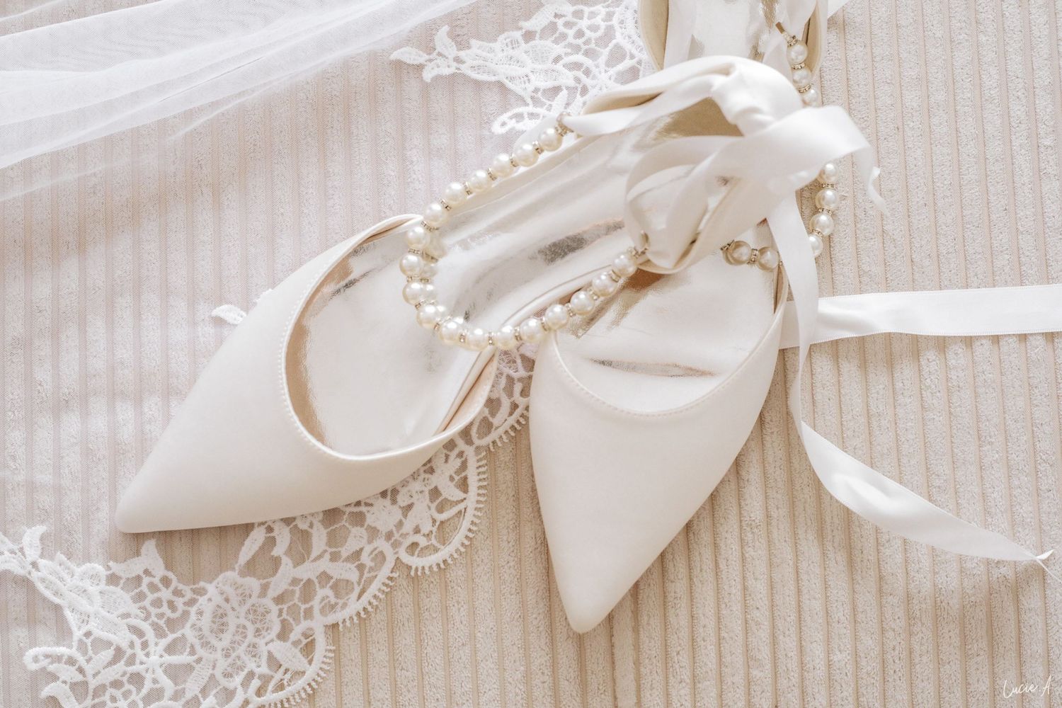 Escarpins de mariée élégants en satin blanc, ornés d'un bracelet de perles et d'un nœud en ruban sur un fond de dentelle ivoire délicate.