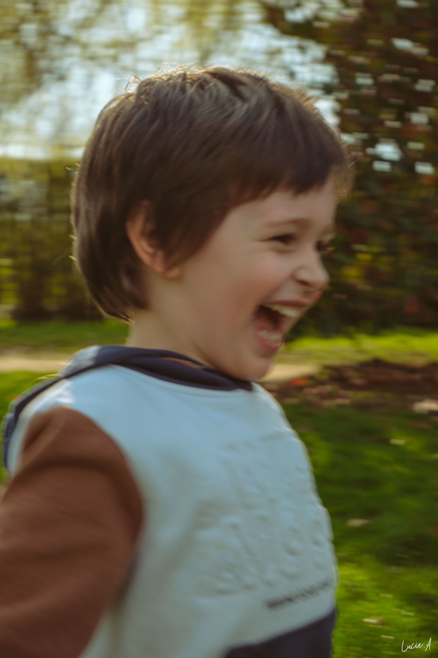 Portrait de profil en couleur d'un jeune garçon riant avec toutes ses dent dans un parc à Lille