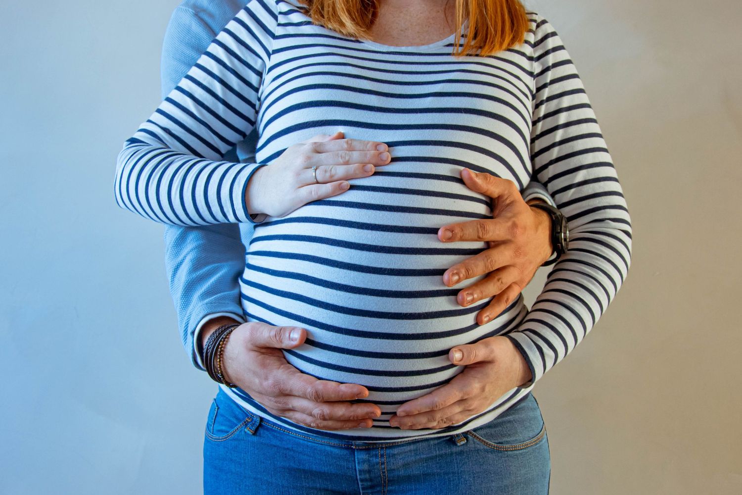 Gros plan couleur lors d'une séance grossesse, l'homme se tient derrière la femme, les mains sous son ventre, prise à Ronchin