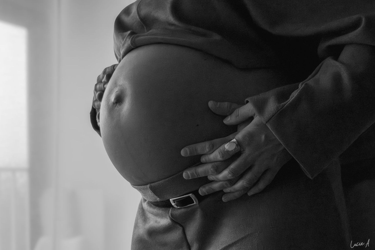 Gros plan noir et blanc d’une femme enceinte tenant son ventre avec les mains de son compagnon
