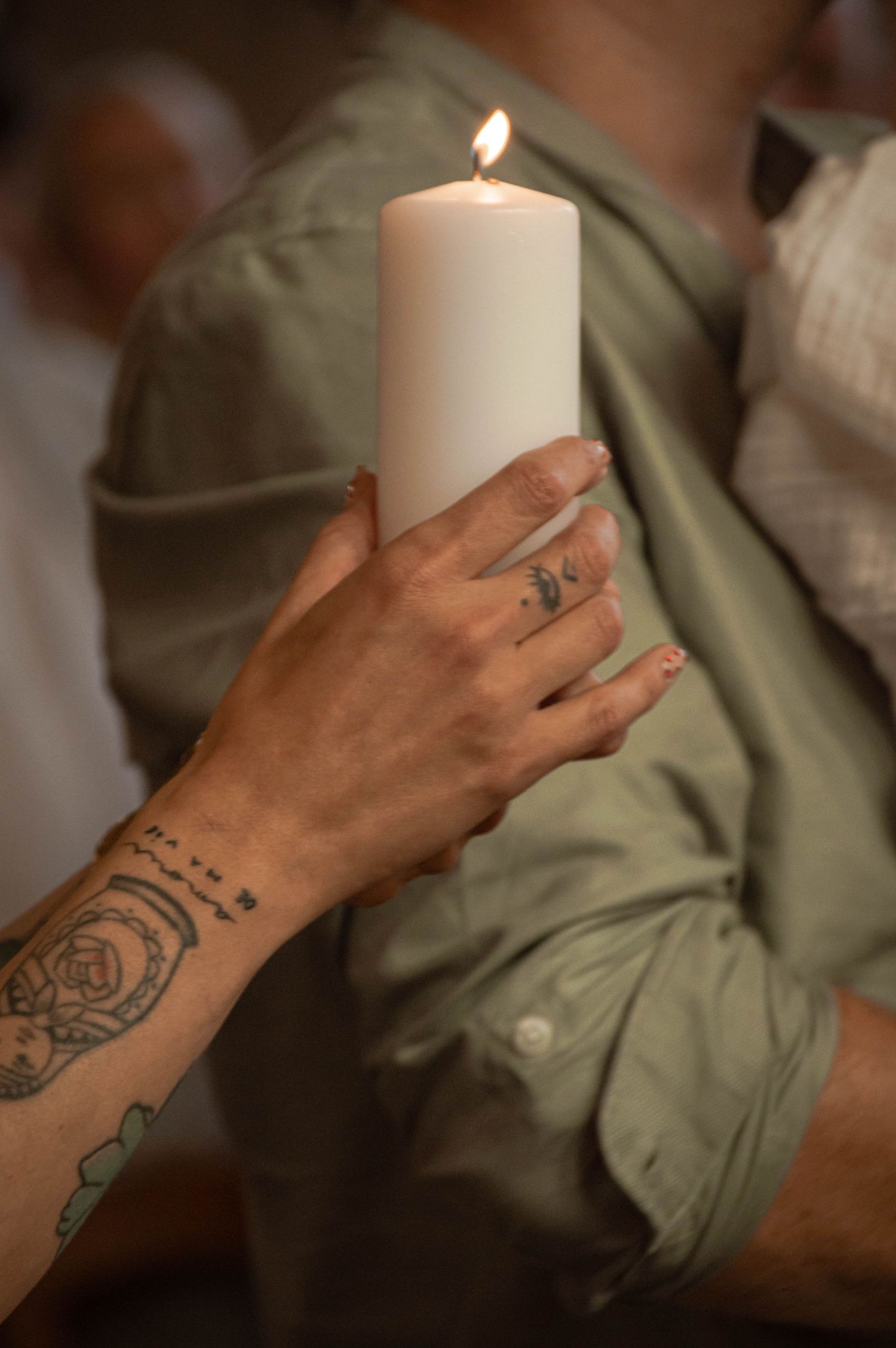 Prise couleur d'une main tatouée tenant une bougie lors d'une séance baptême à Ronchin