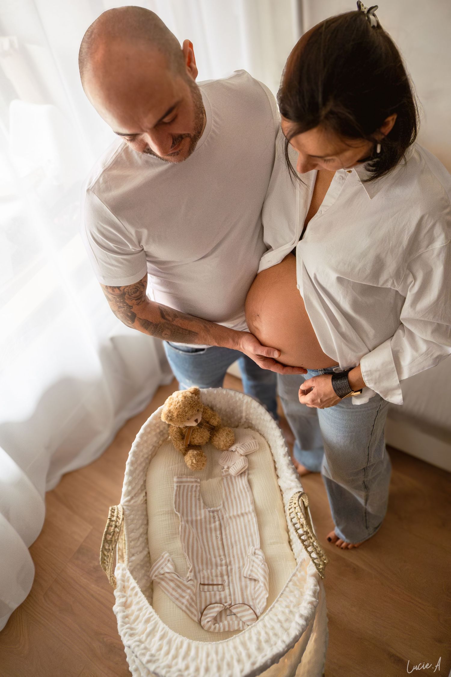 Un couple attendant un enfant caresse tendrement le ventre de la femme enceinte près d'un berceau avec un ours en peluche dans une chambre