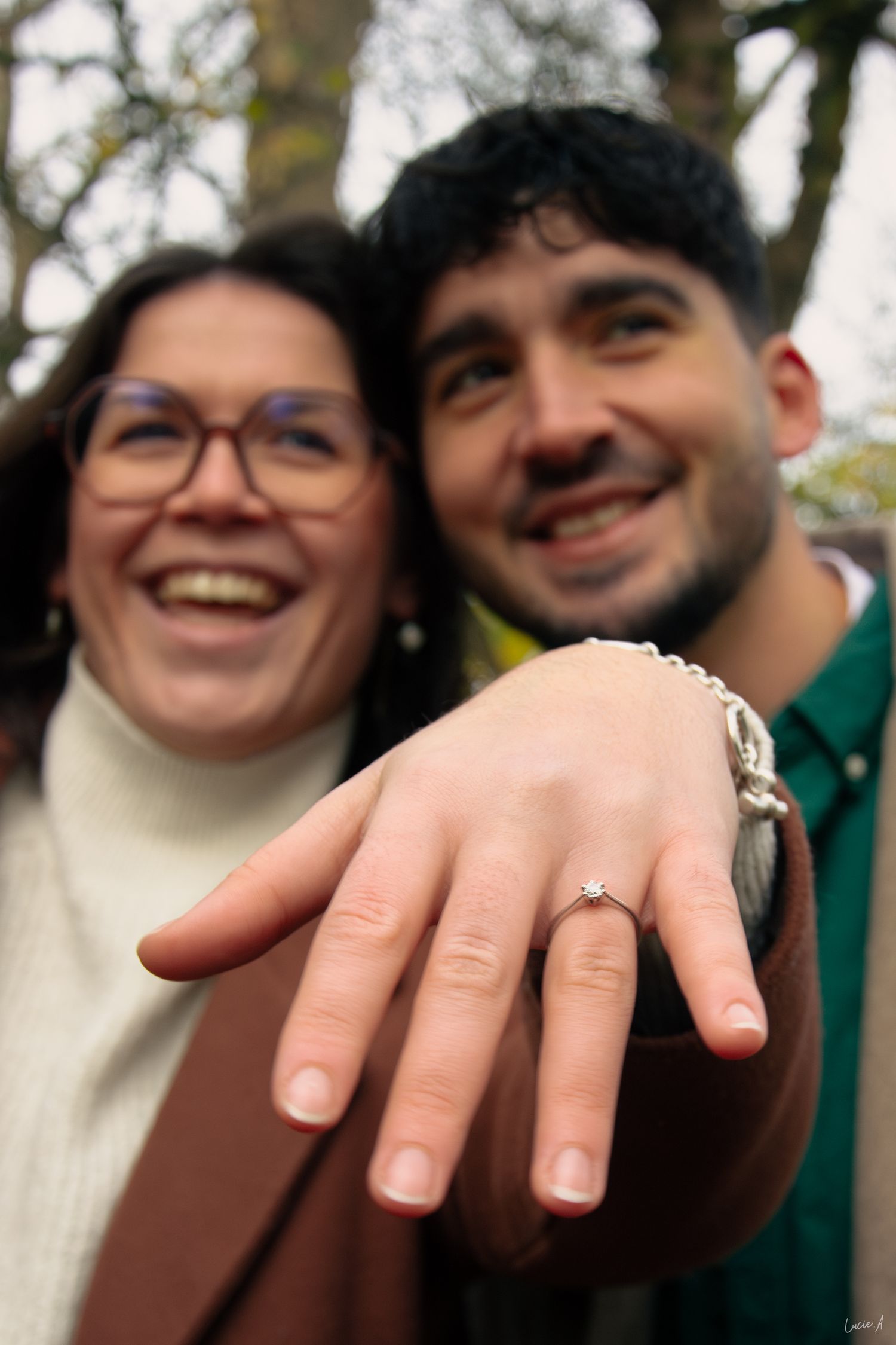 Portrait couleur et arrière flou, couple se tenant cote à cote avec la main montrant la bague au premier plan, capté en extérieur à Lille