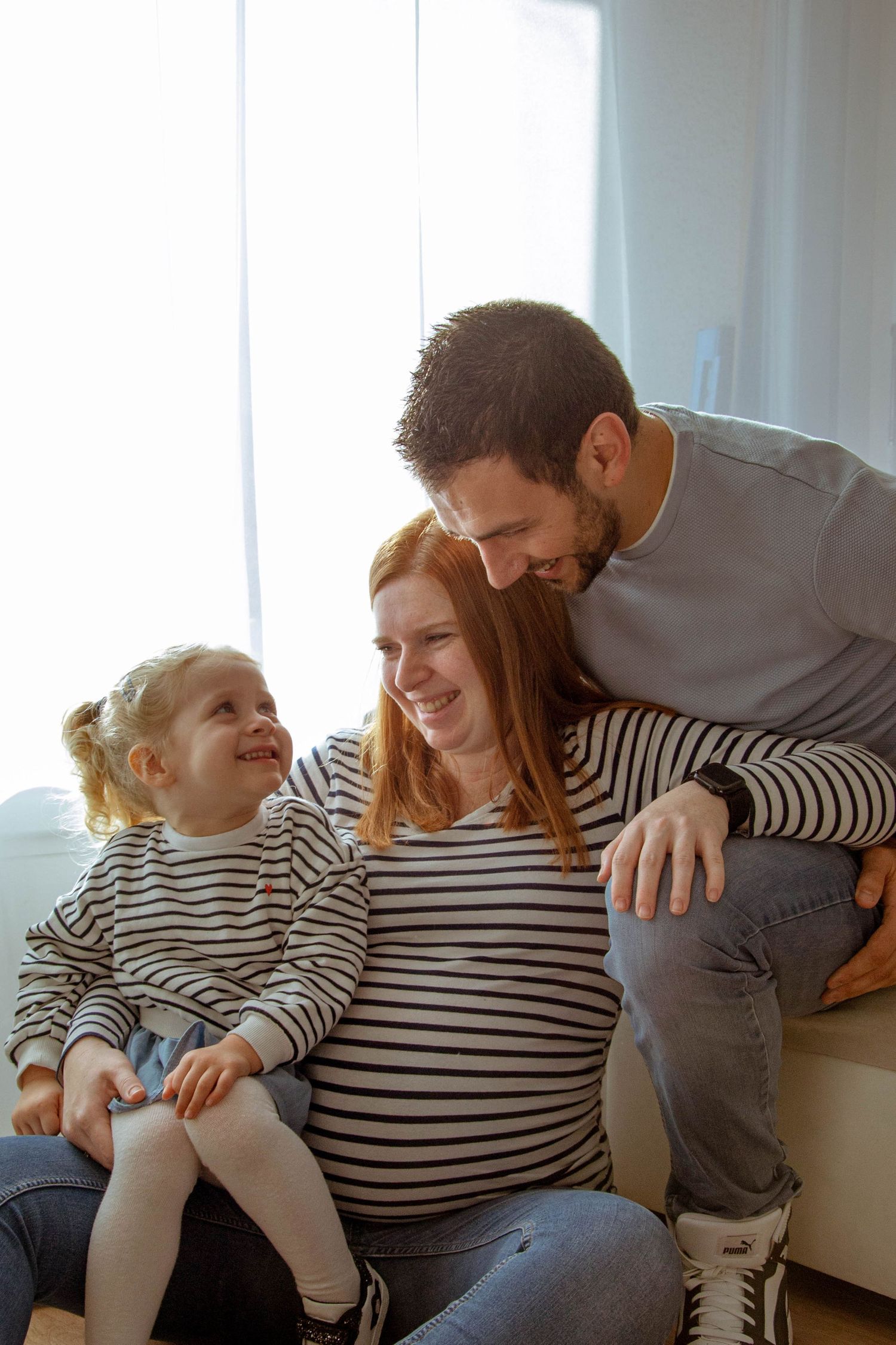 Portrait famille couleur d'une séance grossesse, fille, père et mère sont assis et se regardent en souriant, prise à Ronchin