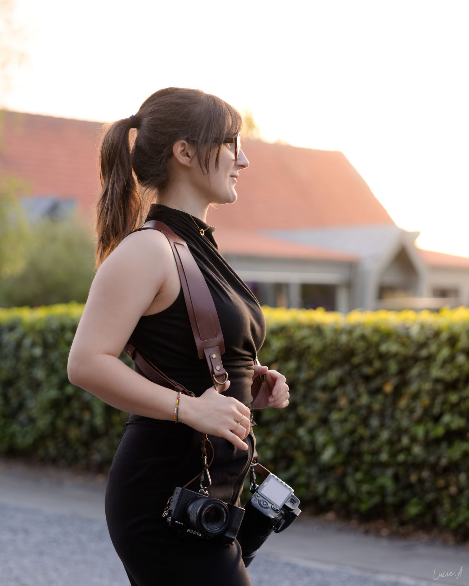La photographe en prestation, tenant un appareil photo reflex numérique en extérieur, à la lumière dorée du crépuscule.