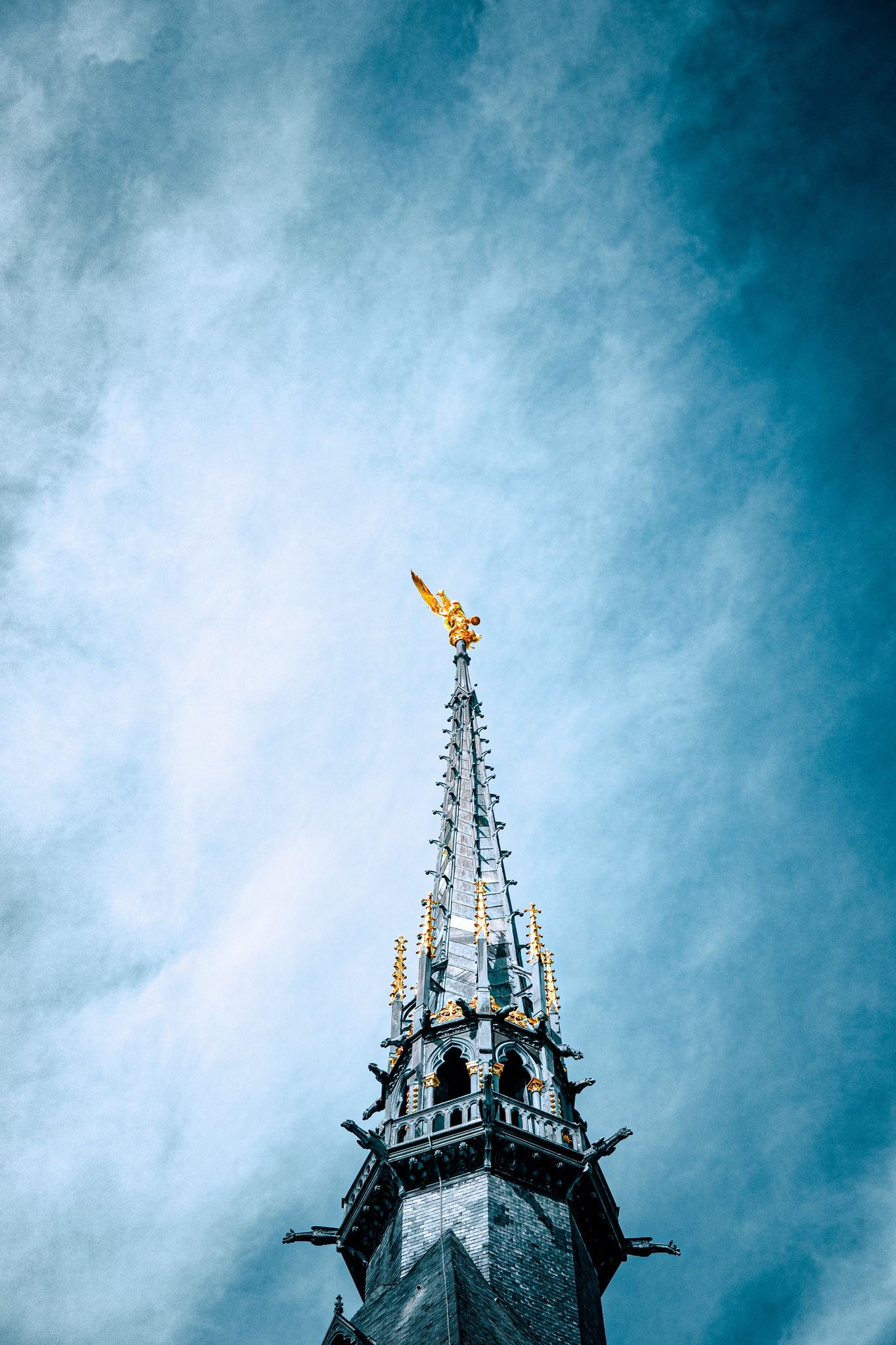 Flèche d'église gothique aux détails dorés, photographiée sur un ciel bleu