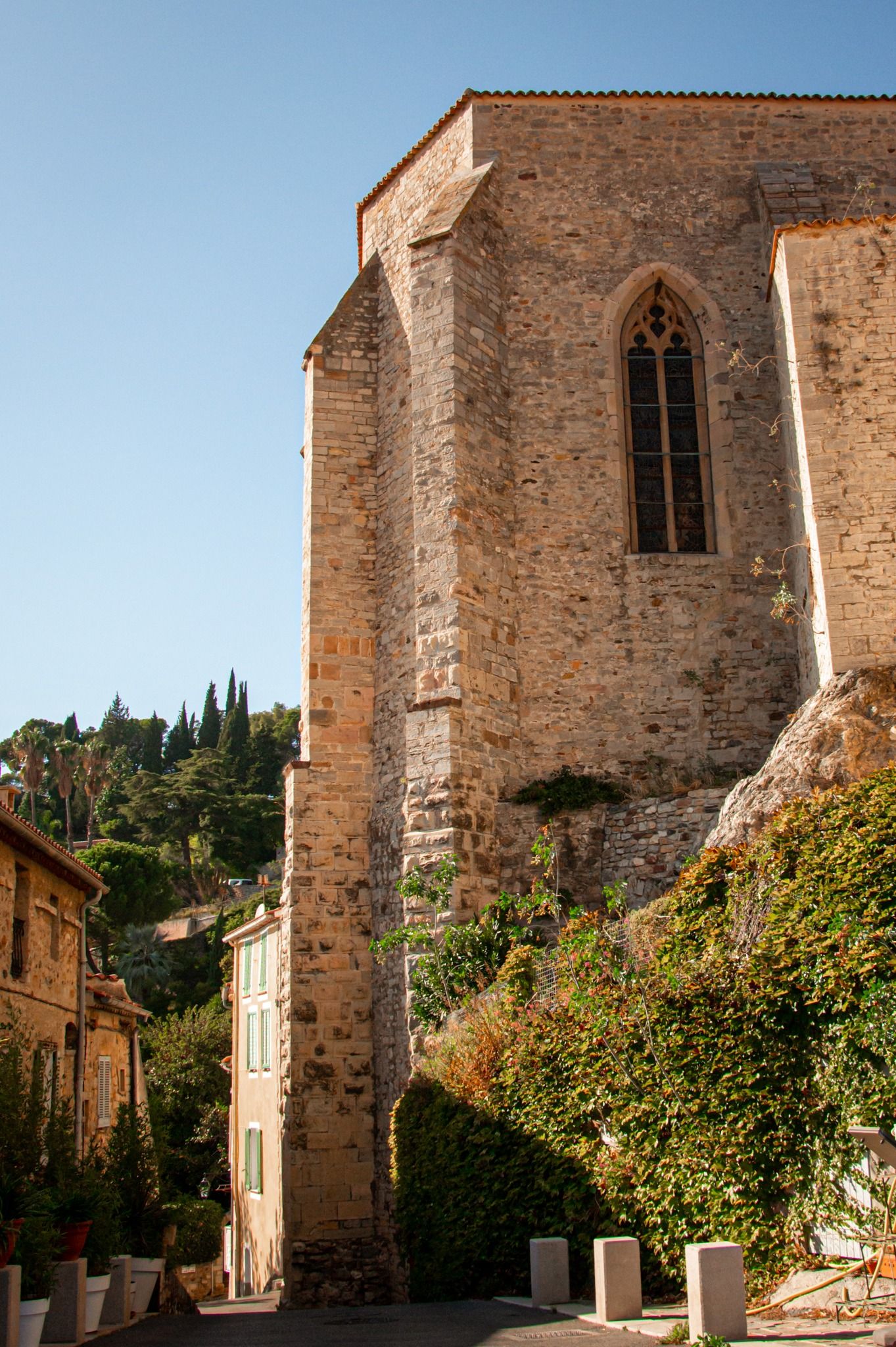 Prise couleur d'une église ancienne en pierre aux fenêtres gothiques, entourée de végétation méditerranéenne