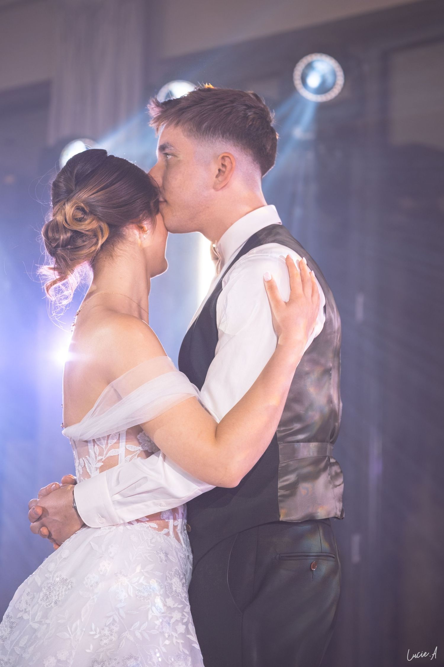 Les mariés échangent un baiser romantique pour leur première danse lors de leur réception de mariage, sous une douce lumière violette.
